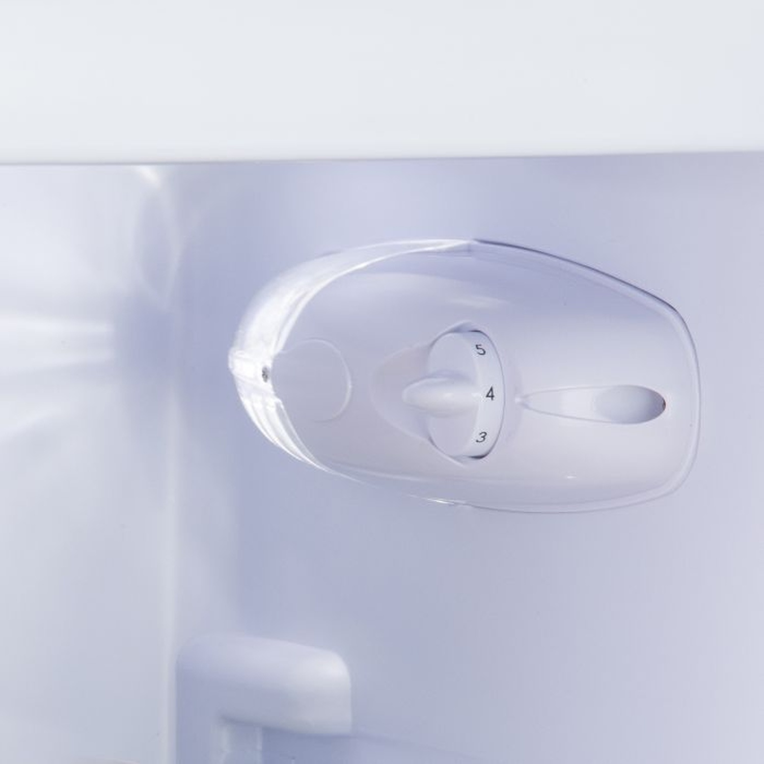 À l'intérieur d'un réfrigérateur blanc, un panneau de contrôle en plastique transparent avec un cadran numéroté de 3 à 5. Le fond est blanc.