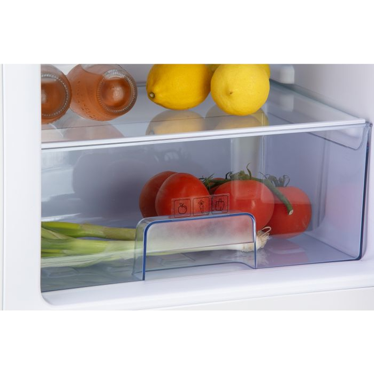 À l'intérieur d'un réfrigérateur : on voit des citrons, des tomates, des oignons verts et des bouteilles de boissons. Les articles sont rangés dans des récipients en plastique transparent.