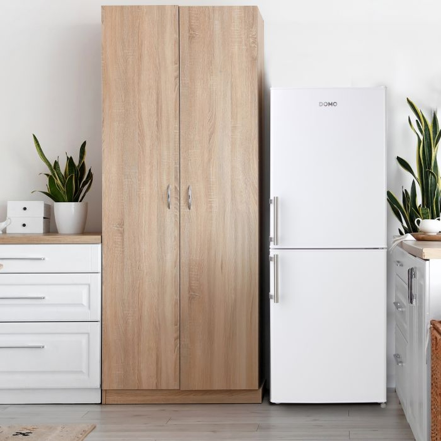 Un réfrigérateur blanc avec une armoire en bois et des tiroirs blancs. Des plantes en pots et un mur blanc en arrière-plan.