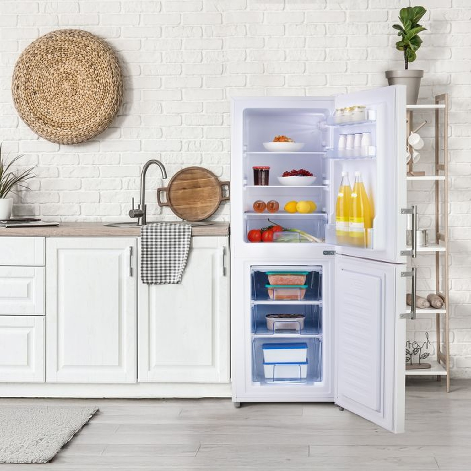 Réfrigérateur ouvert avec nourriture, cuisine avec mur de briques blanches, étagères en bois avec plante, décor en osier, armoires blanches et sol.