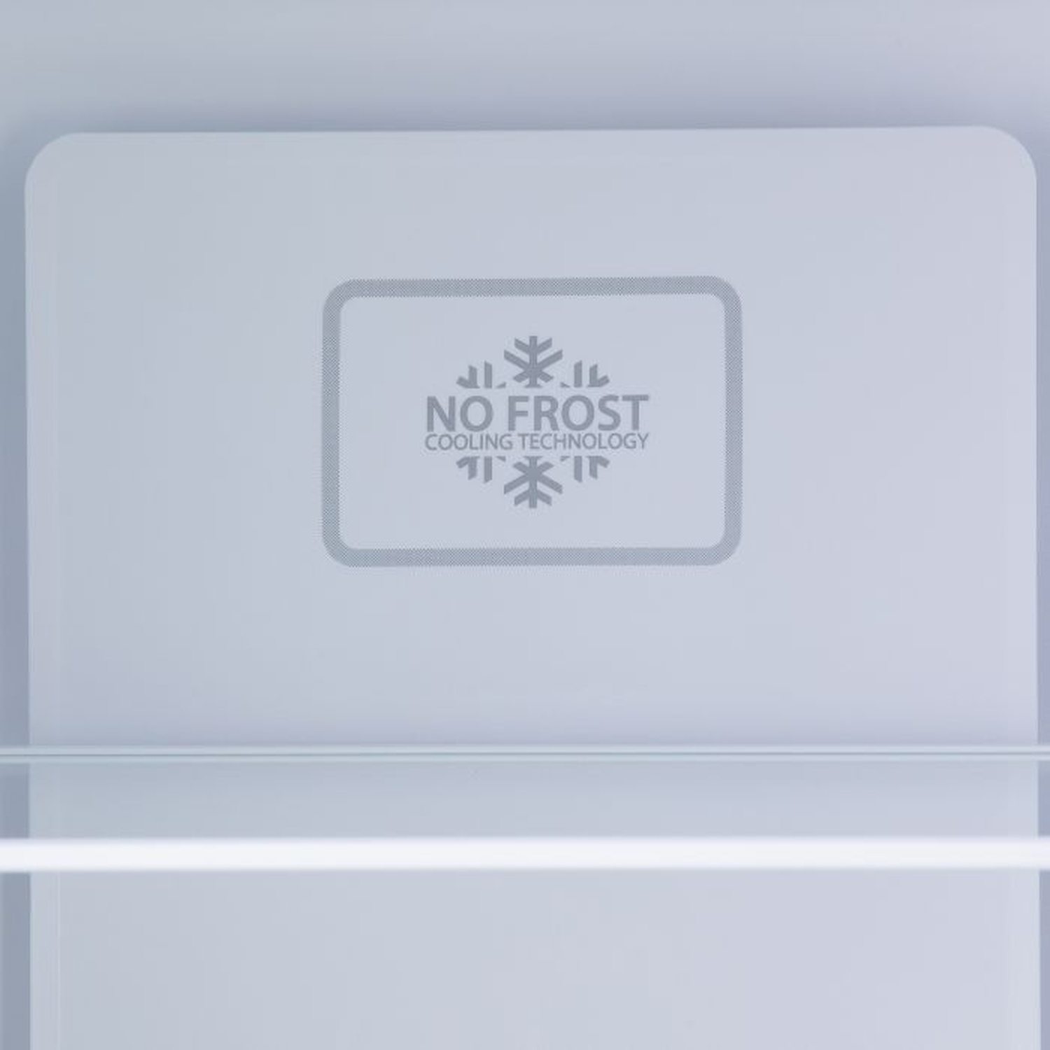 À l'intérieur d'un réfrigérateur. Le panneau supérieur porte le logo 'No Frost'. Il y a une étagère en verre au milieu.