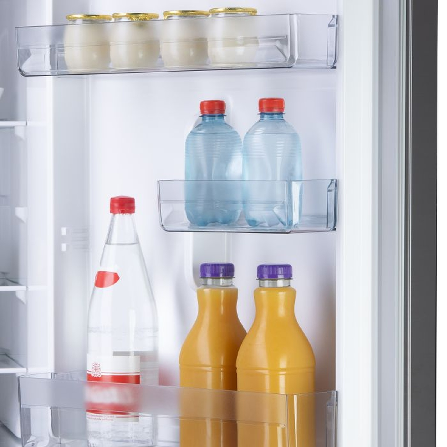 À l'intérieur d'un réfrigérateur: bouteilles d'eau, jus et yaourts. Le réfrigérateur est blanc avec des étagères transparentes. Les bouteilles ont des bouchons rouges et violets.