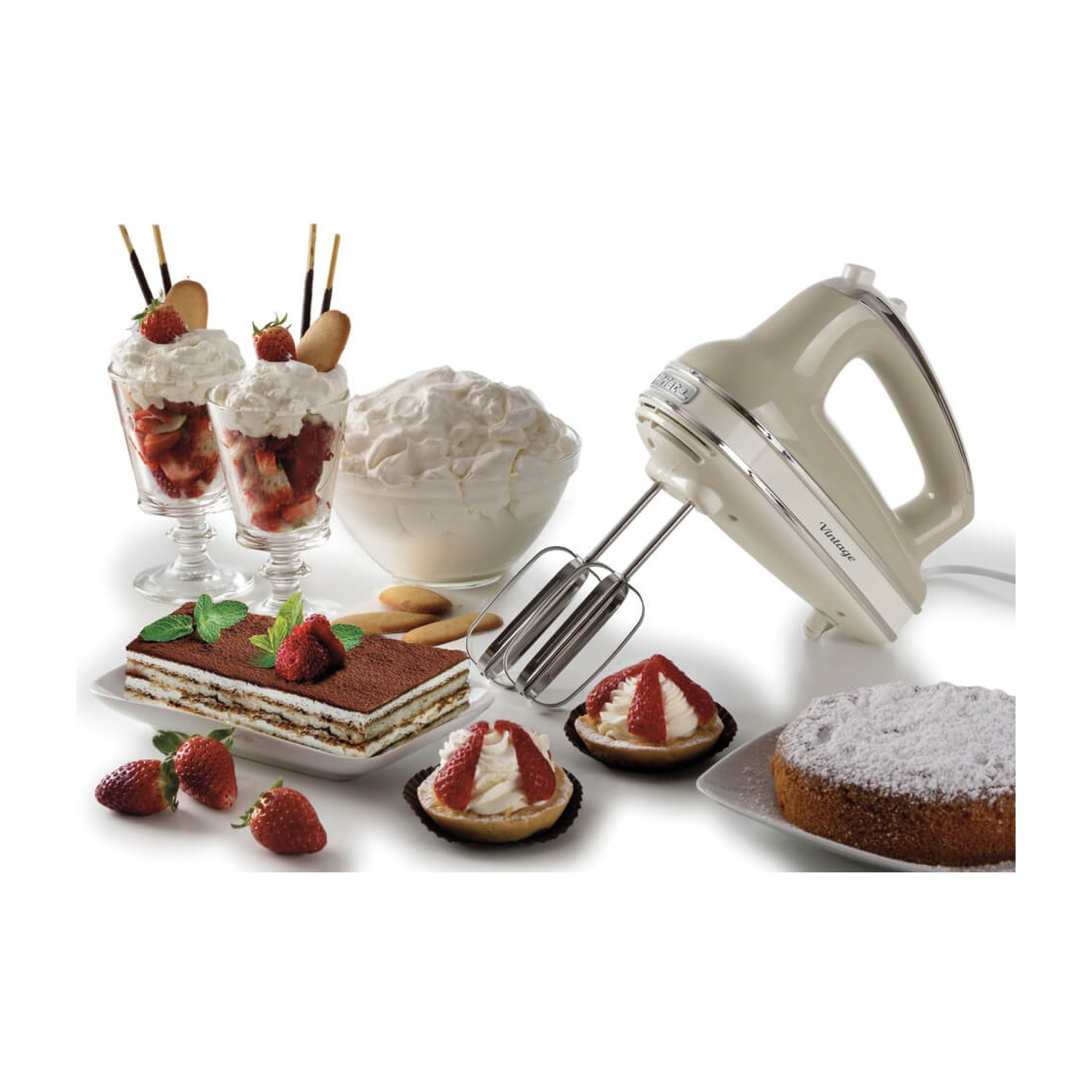Un frullatore a mano beige accanto a dessert, tra cui parfait alle fragole, tiramisù, crostatine, torta e panna montata, su una superficie bianca.