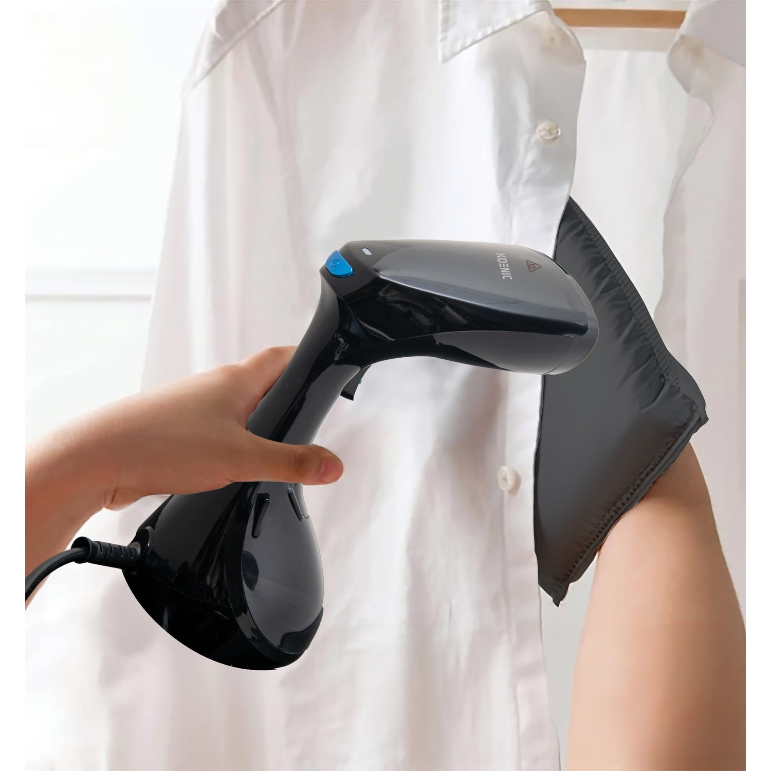 Una persona che stira una camicia bianca con un vaporizzatore nero. La camicia è appesa a un appendiabiti. Una manica nera è sul braccio.