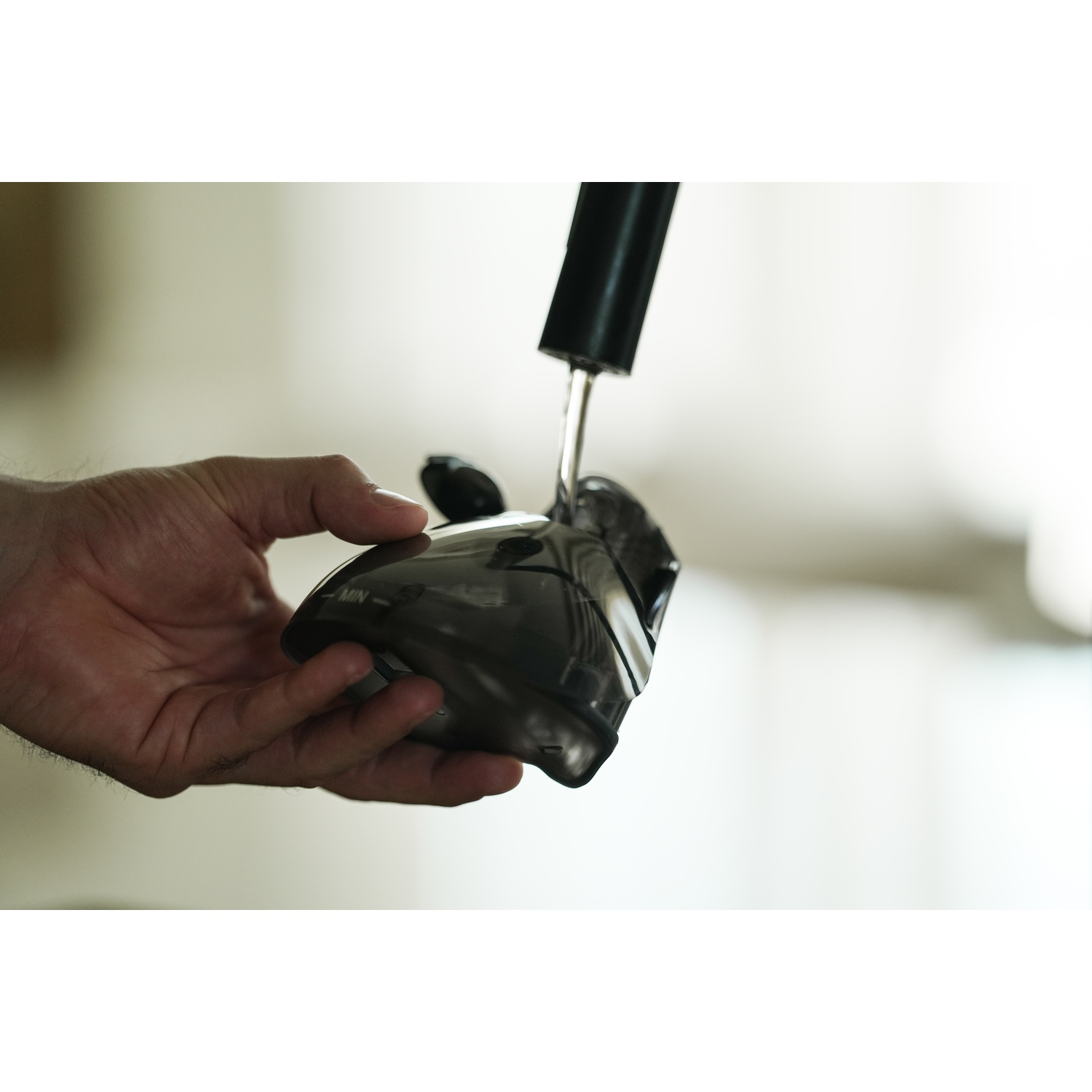 Una mano tiene in mano un dispositivo nero, forse un mouse o parte di una macchina. Un tubo nero è sopra. Lo sfondo è sfocato.