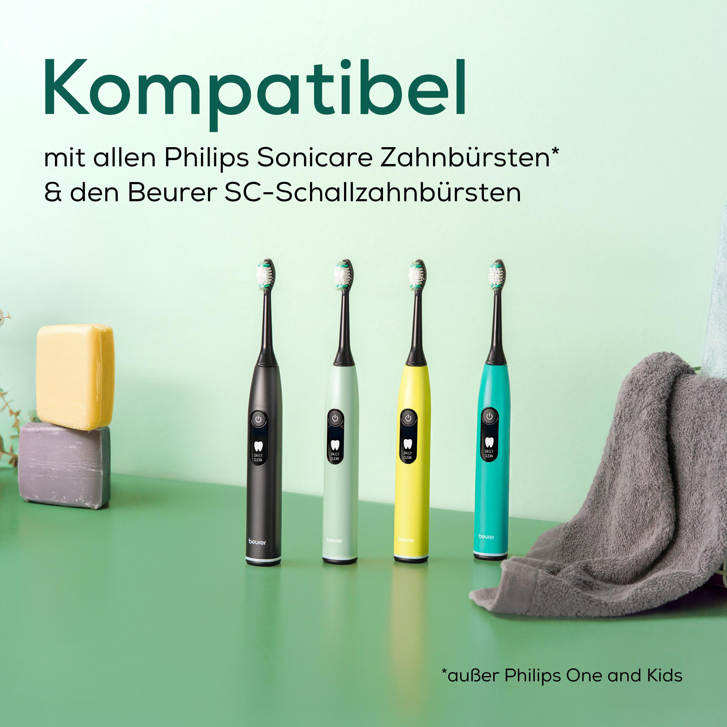 Vier bunte elektrische Zahnbürsten werden auf einer grünen Oberfläche gezeigt. Ein Handtuch und Seife sind im Hintergrund.