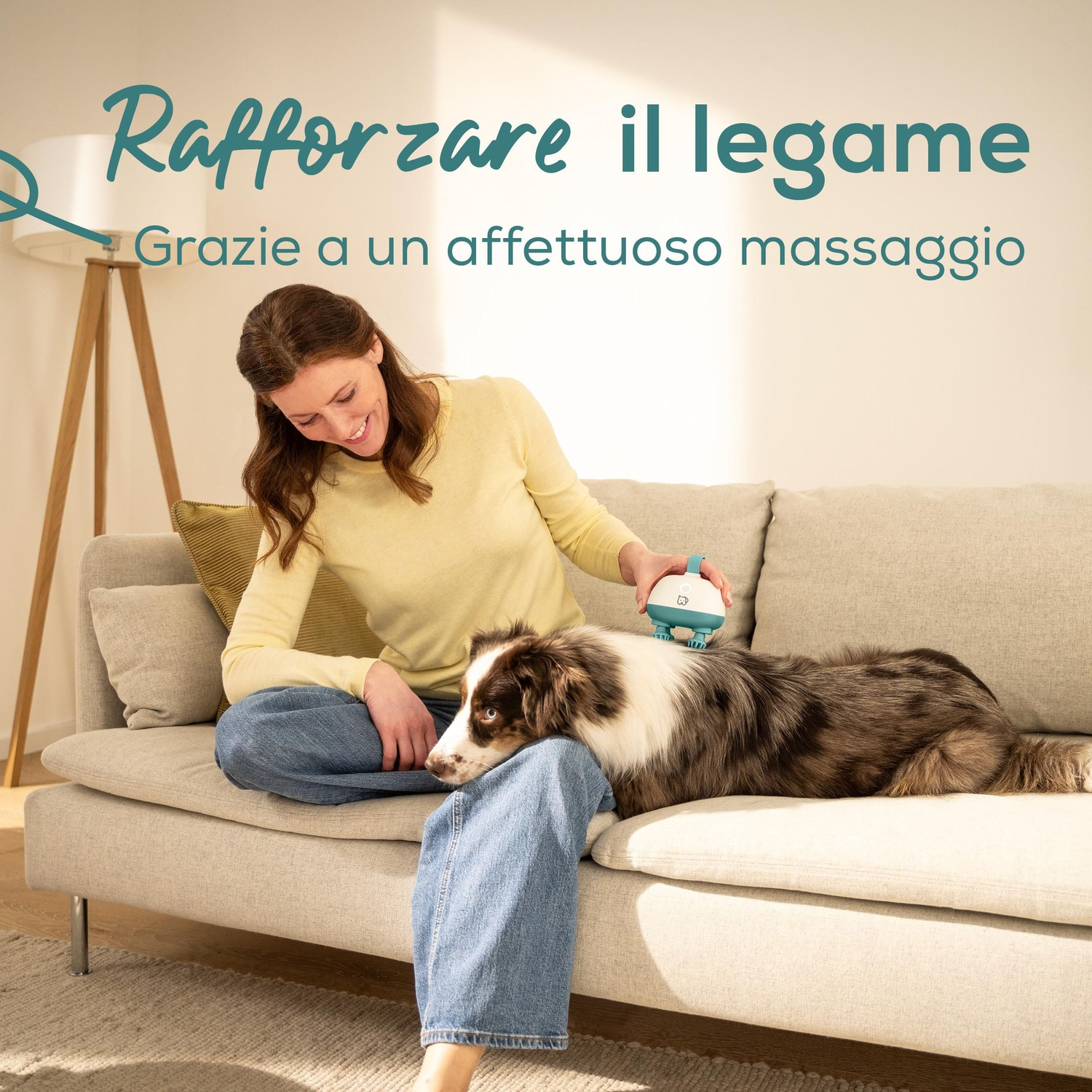 Una donna massaggia un cane con un dispositivo blu e bianco. Sono su un divano. Il testo dice: 'Rafforzare il legame'.