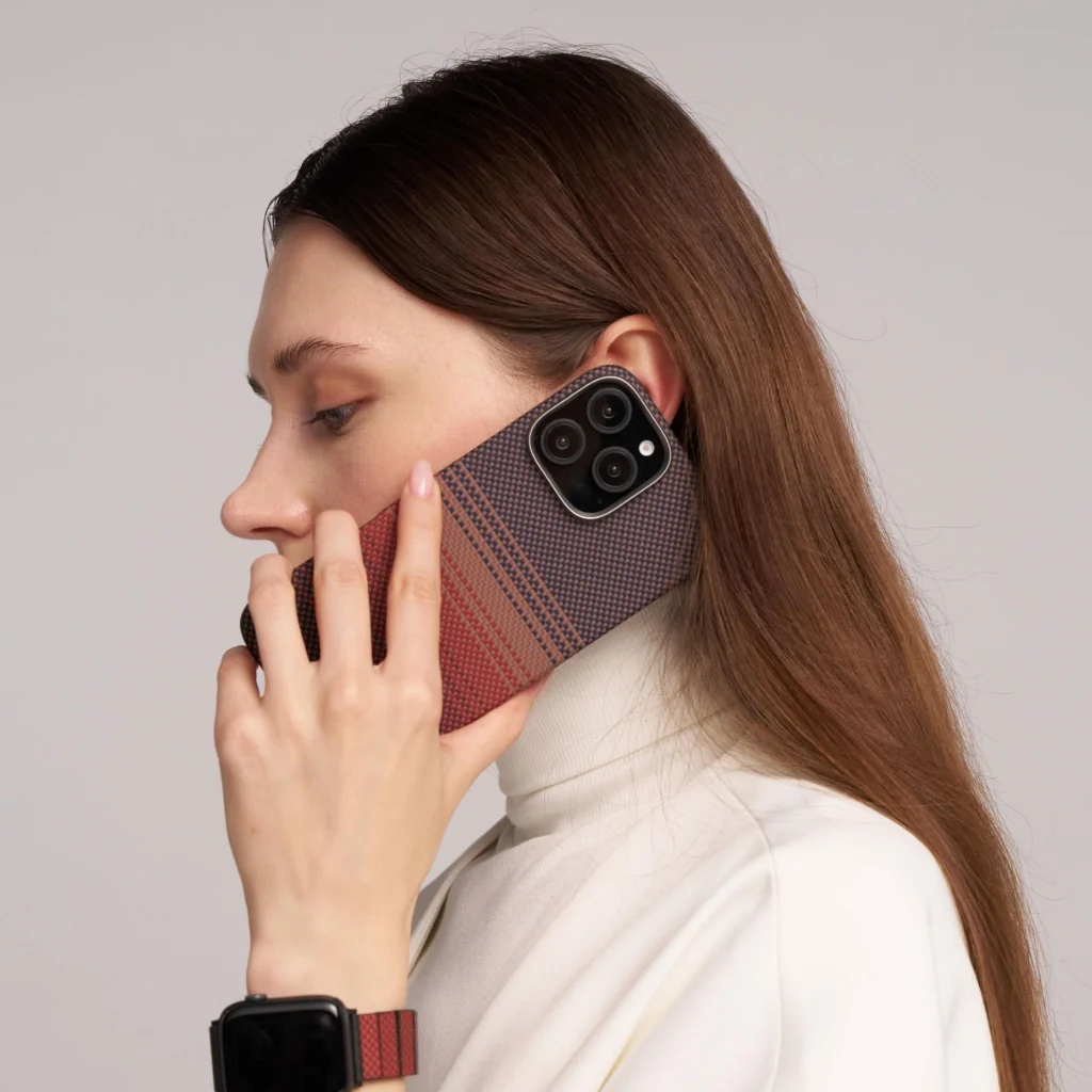 Egy nő a füléhez tart egy telefont. Fehér garbót visel, és van egy órája. A telefontok színátmenetes.