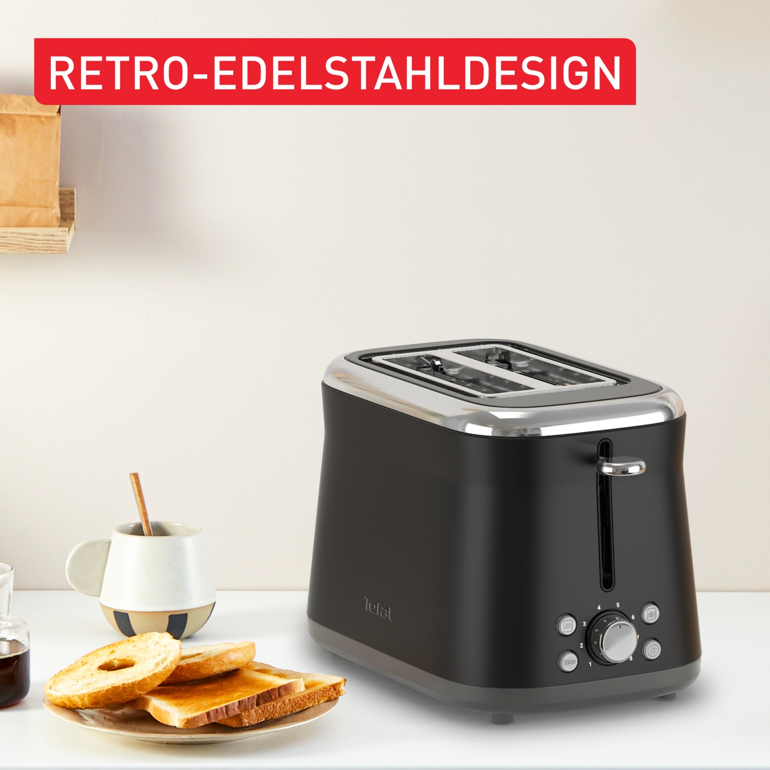 A black Tefal toaster with stainless steel accents sits on a white surface. Toasted bread and a mug are on the left.