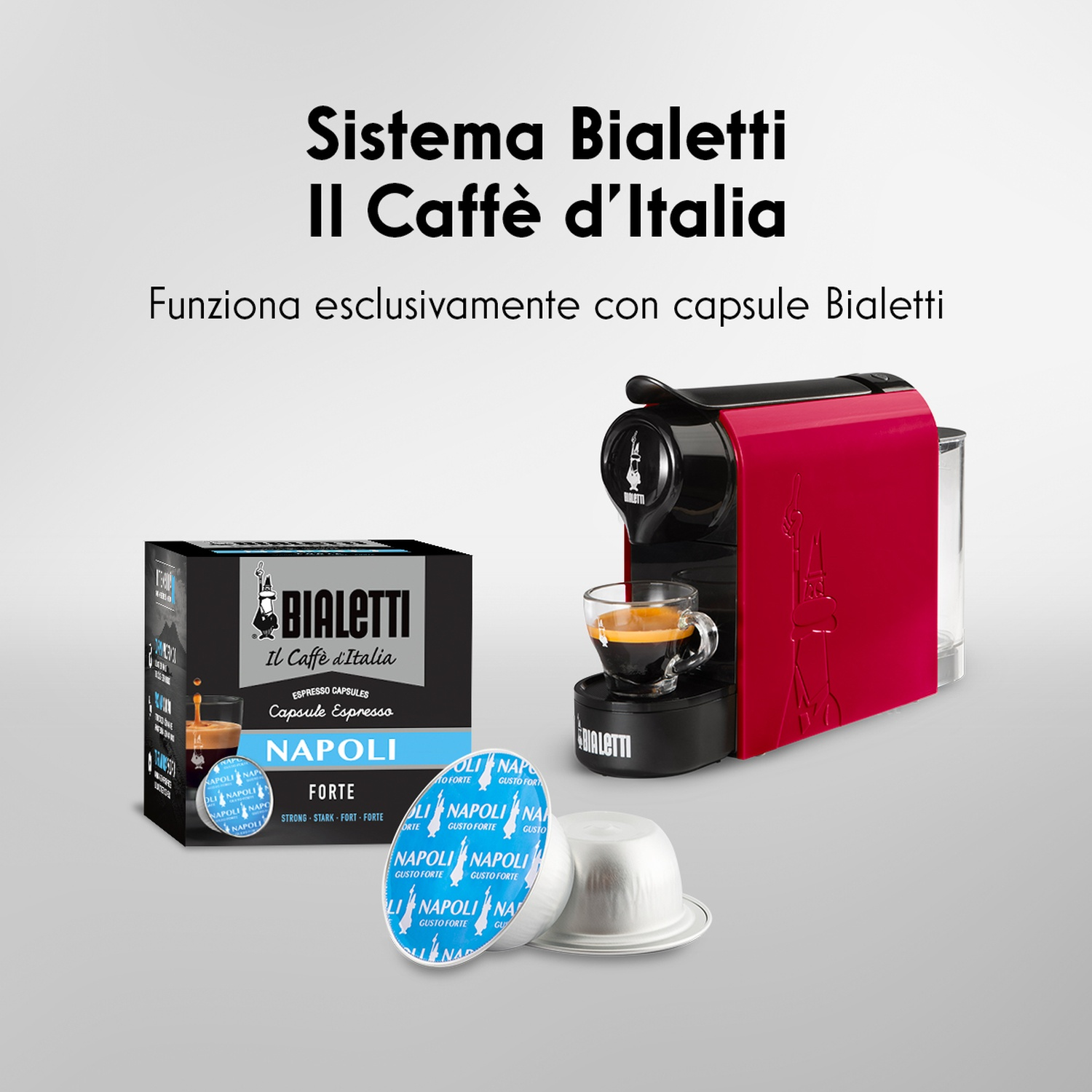 Una macchina da caffè Bialetti rossa con una tazza di caffè, capsule di caffè e una scatola di capsule sul tavolo.