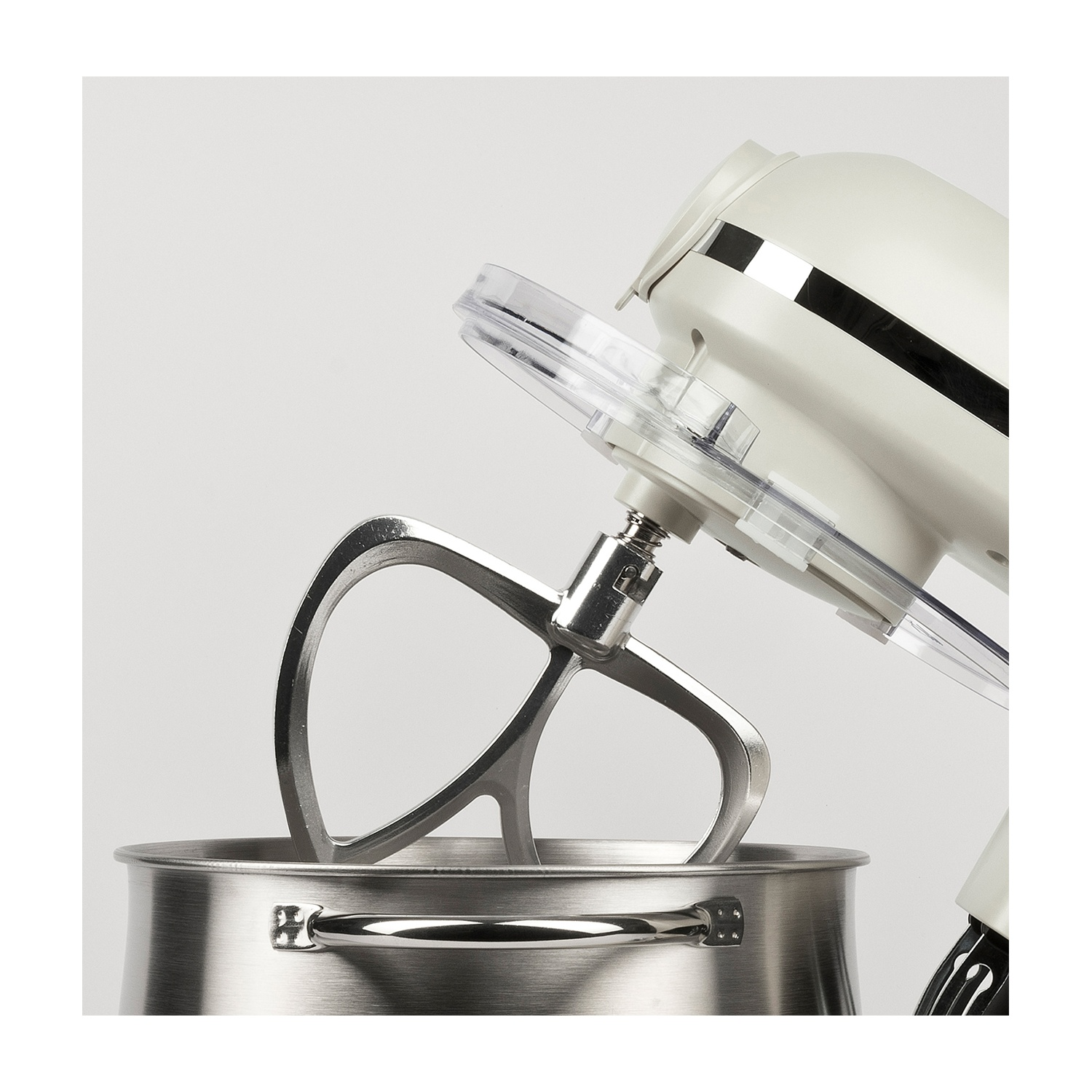 Primo piano di un mixer da cucina. Il mixer è bianco sporco con dettagli cromati. Sotto c'è una ciotola in acciaio inossidabile.