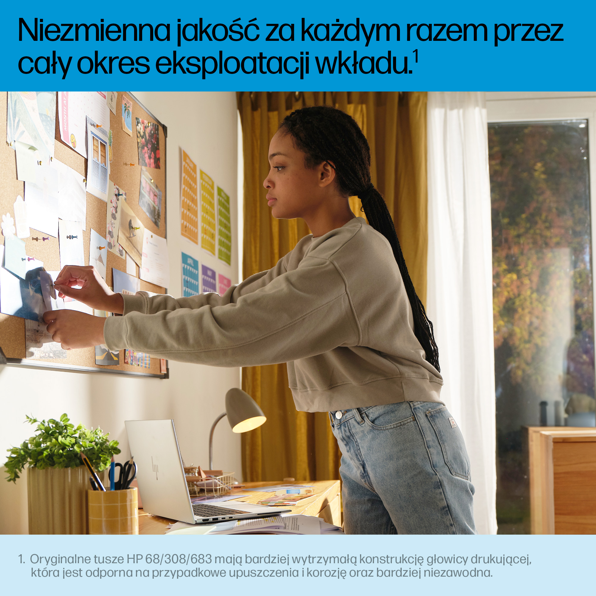 Kobieta przypina zdjęcie do tablicy korkowej. Na biurku stoi laptop i lampa. W tle widać okno i roślinę.