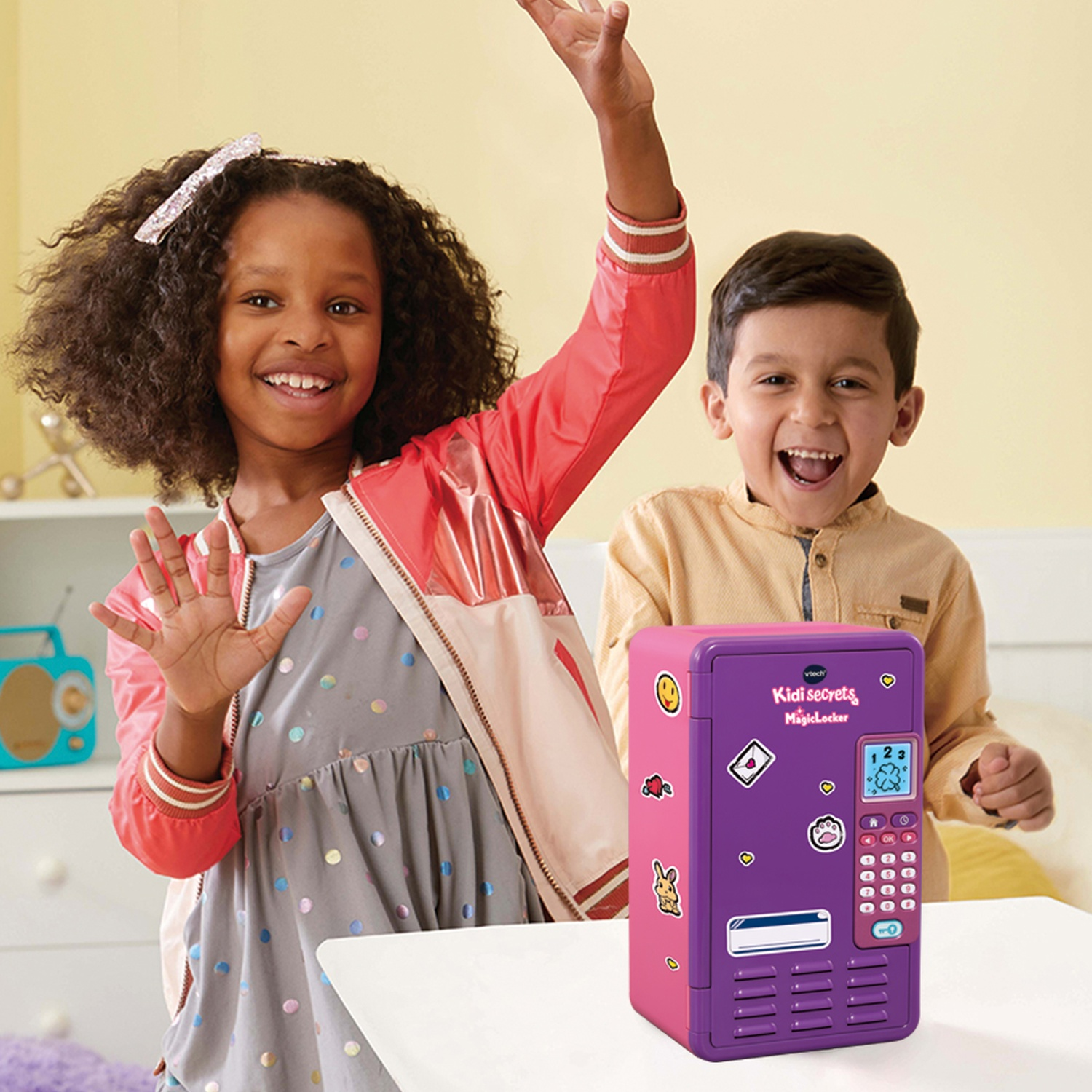 Due bambini sorridenti con un armadietto giocattolo viola e rosa. Un bambino alza la mano. L'armadietto ha adesivi e una tastiera.