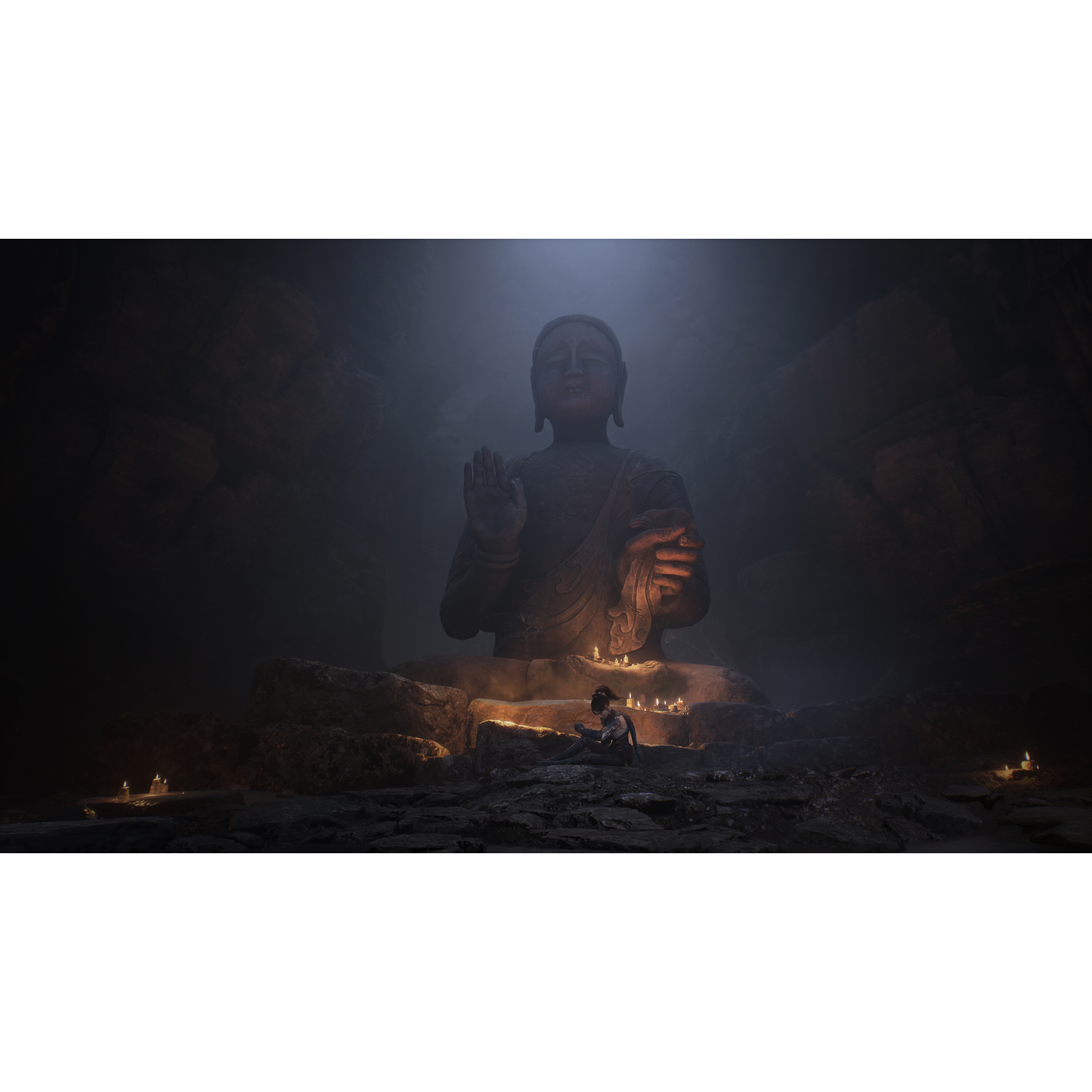 Une grande statue de Bouddha dans une grotte. Une personne est assise devant, entourée de bougies. Une lumière faible illumine la scène, créant des ombres.