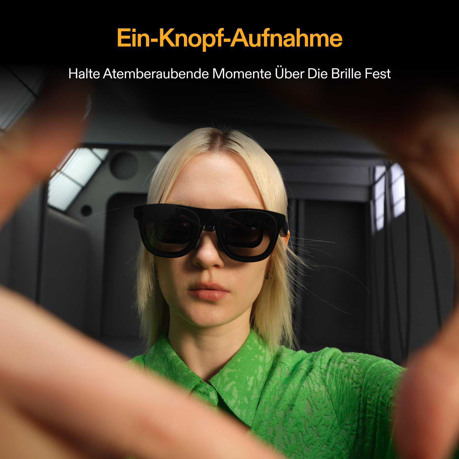 Eine Frau mit Sonnenbrille, die von Händen umrahmt ist. Sie hat blondes Haar und ein grünes Hemd. Der Hintergrund ist ein dunkler Raum.