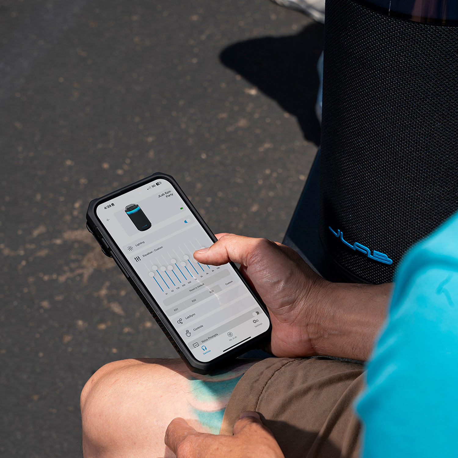 Een persoon gebruikt een telefoon om een ​​luidspreker te bedienen. Het telefoonscherm toont een app-interface met verlichtings- en equalizeropties.