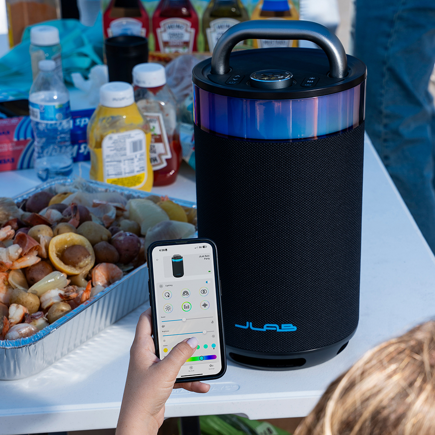Een picknickscène met een luidspreker, eten en een persoon die een smartphone gebruikt om de lichten van de luidspreker te bedienen. Flessen sauzen op de achtergrond.