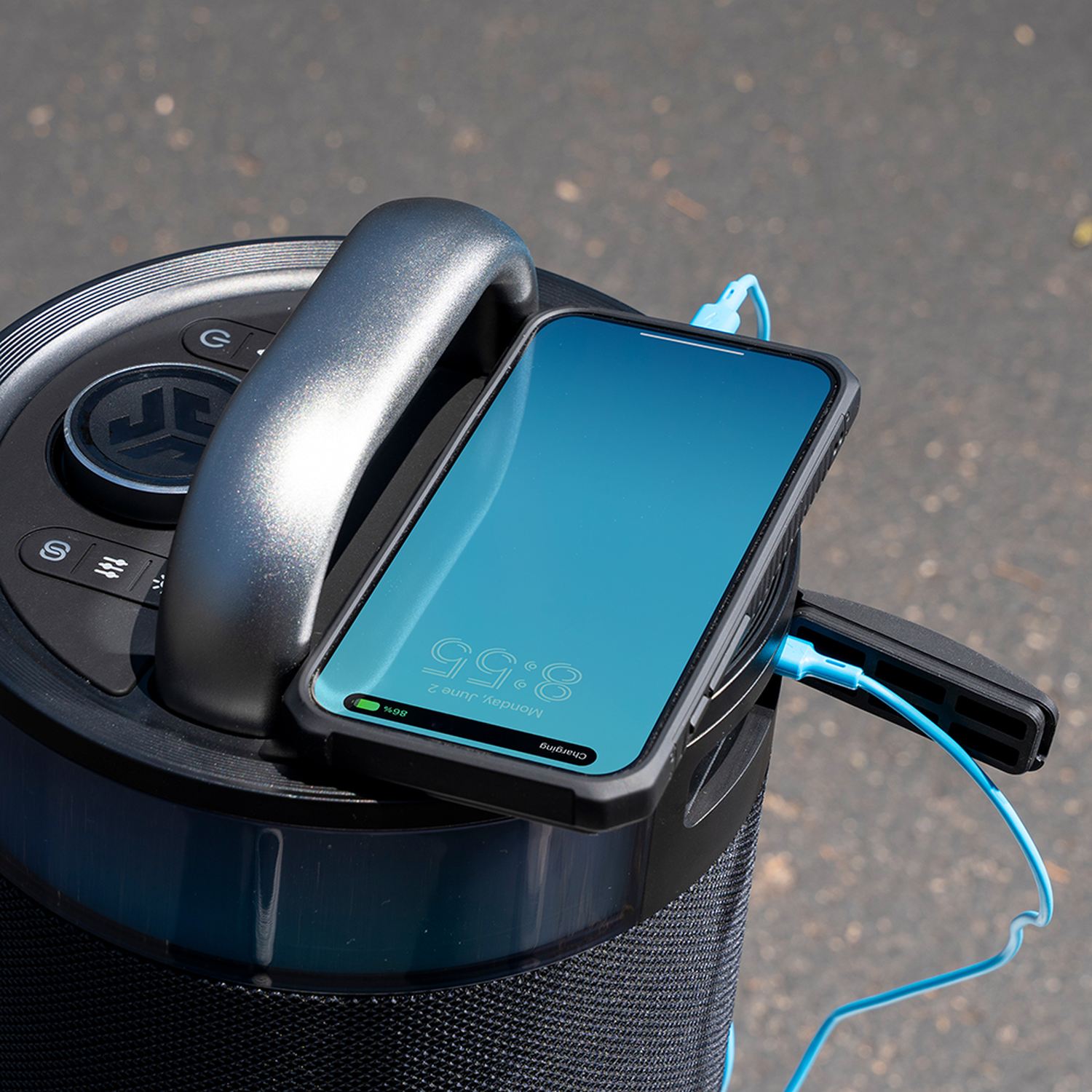 Een telefoon die oplaadt op een luidspreker. De telefoon is zwart met een blauw scherm. De luidspreker is zwart en grijs. Een blauwe kabel verbindt ze.