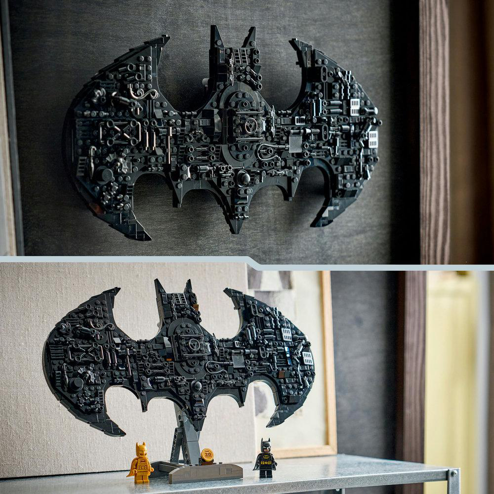 Zwei Batman-Symbole, eines montiert, eines auf einem Ständer mit Figuren. Dunkelgraue, komplexe Lego-Bauten, detaillierter Hintergrund.