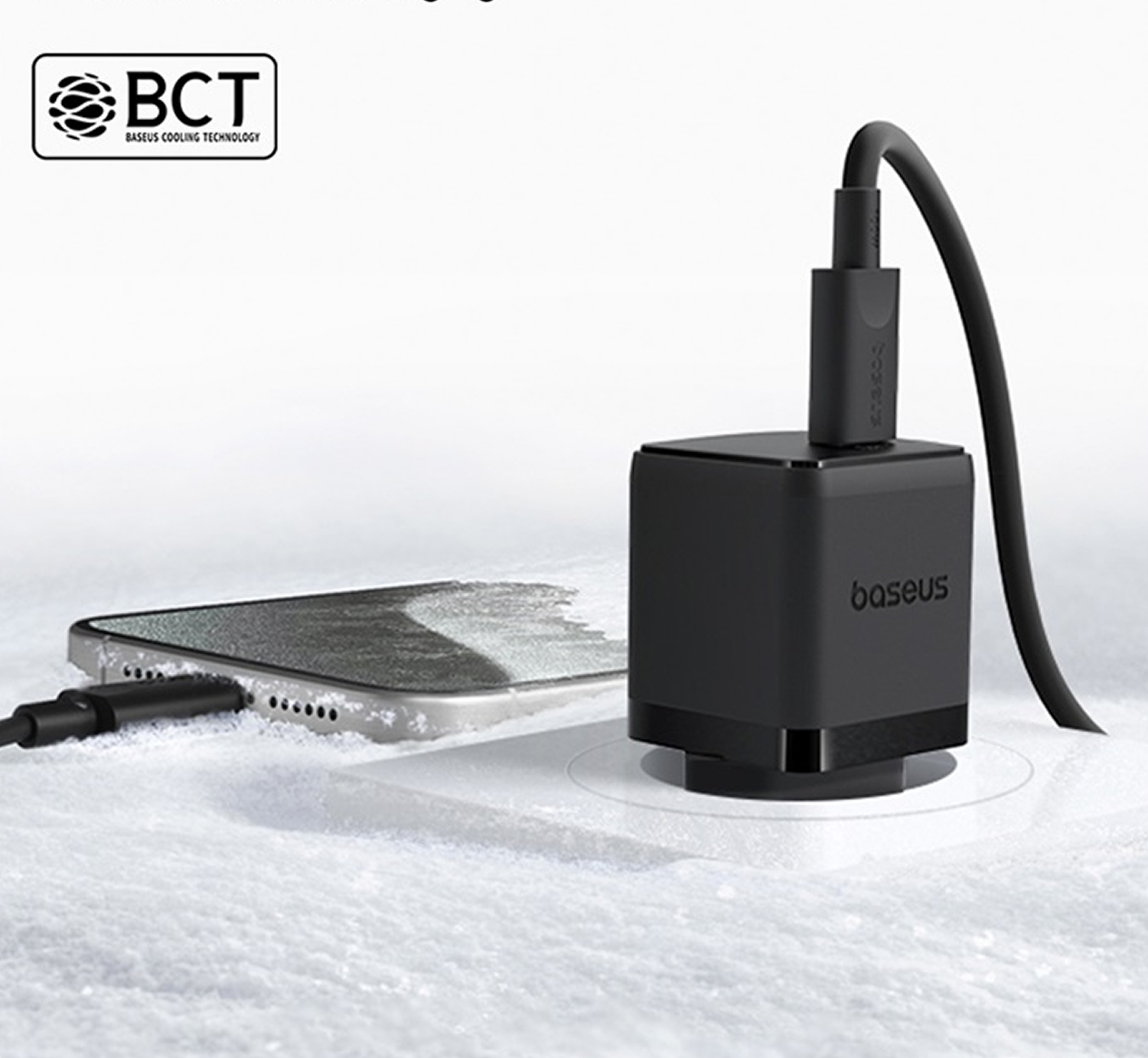 Cargador Baseus negro con cable conectado a un teléfono. La escena está ambientada sobre una superficie blanca y nevada.