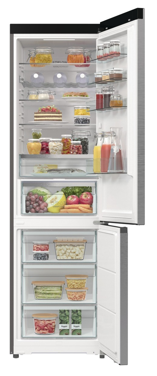 Otwarta lodówka wypełniona jedzeniem: owoce, warzywa, słoiki i napoje. Zamrażarka na dole z większą ilością jedzenia w pojemnikach.