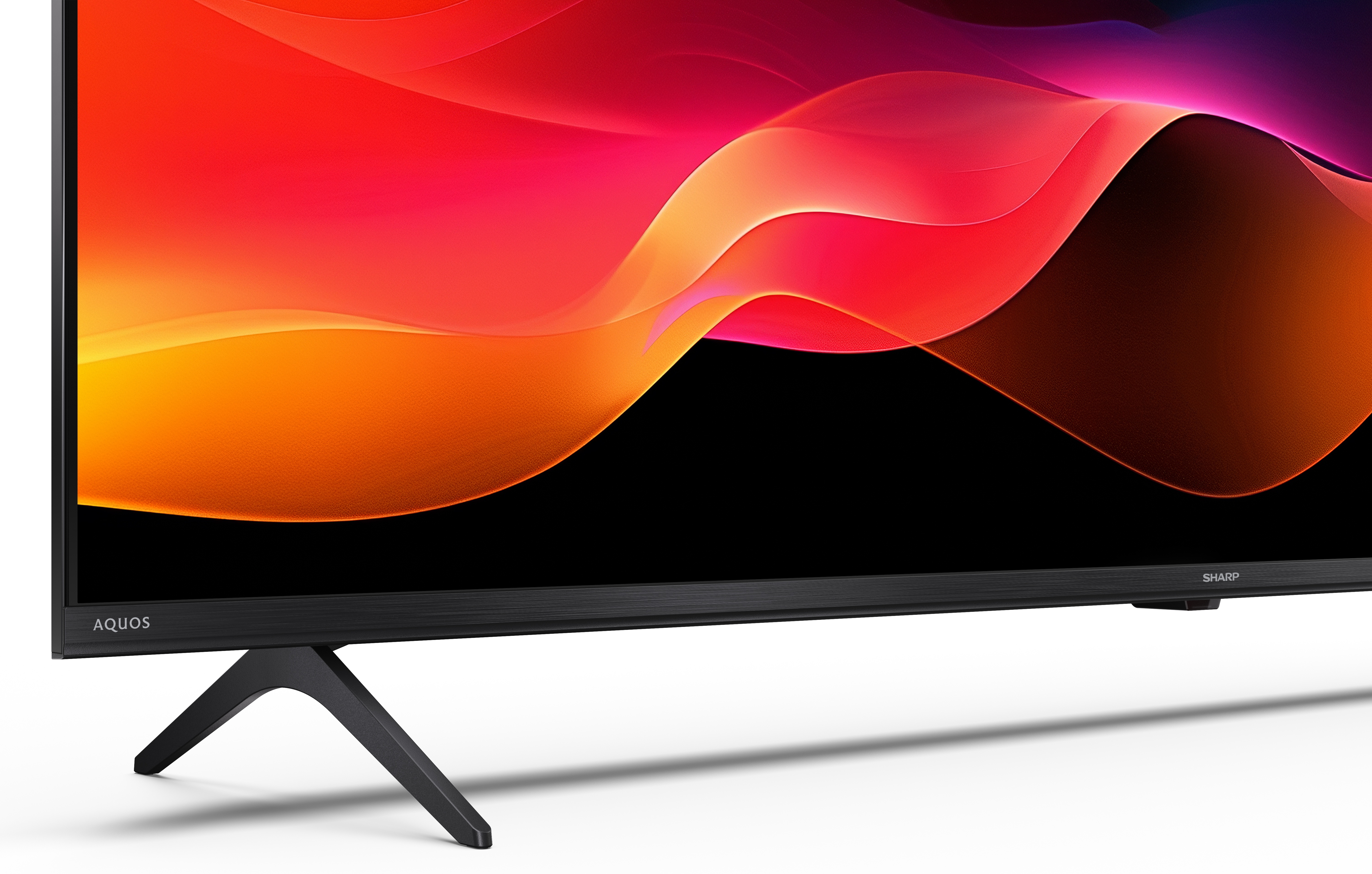 Telewizor Sharp Aquos. Ekran wyświetla kolorowy, abstrakcyjny wzór. Telewizor stoi na białej powierzchni.