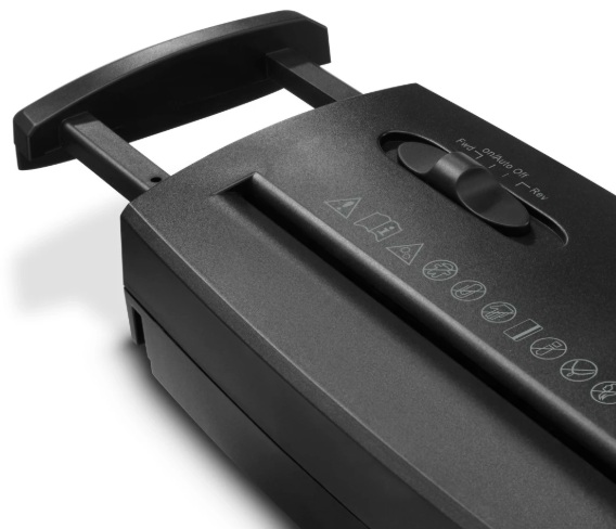 Zbliżenie czarnej niszczarki do papieru. Posiada uchwyt, pokrętło i symbole bezpieczeństwa.