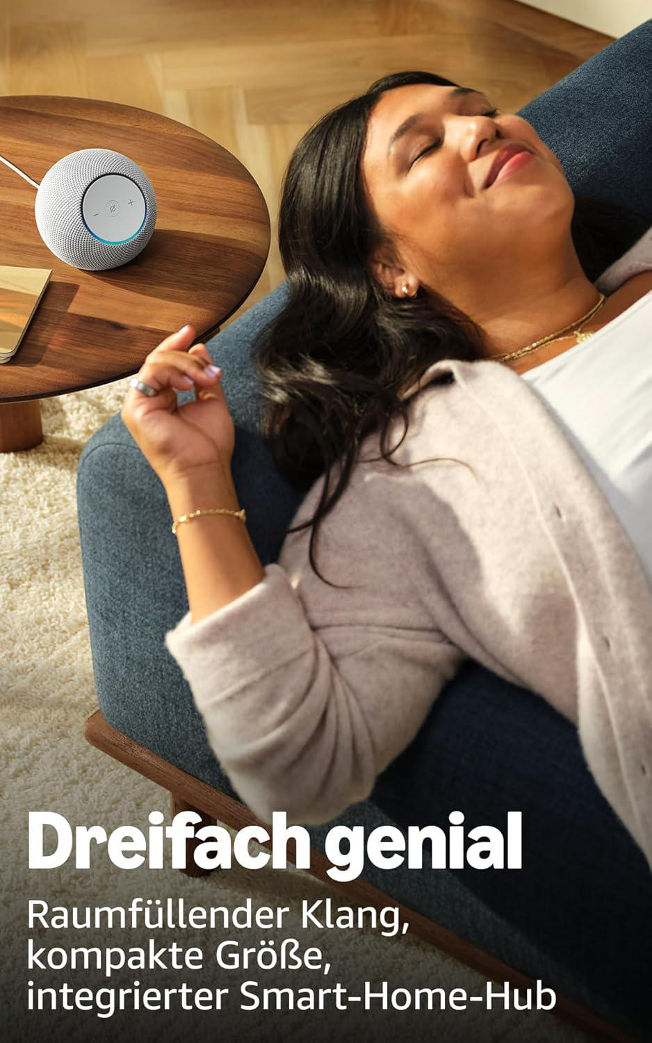 Frau entspannt sich auf blauem Stuhl, neben Holztisch mit Smart-Lautsprecher. Text: Dreifach genial, Raumfüllender Klang.
