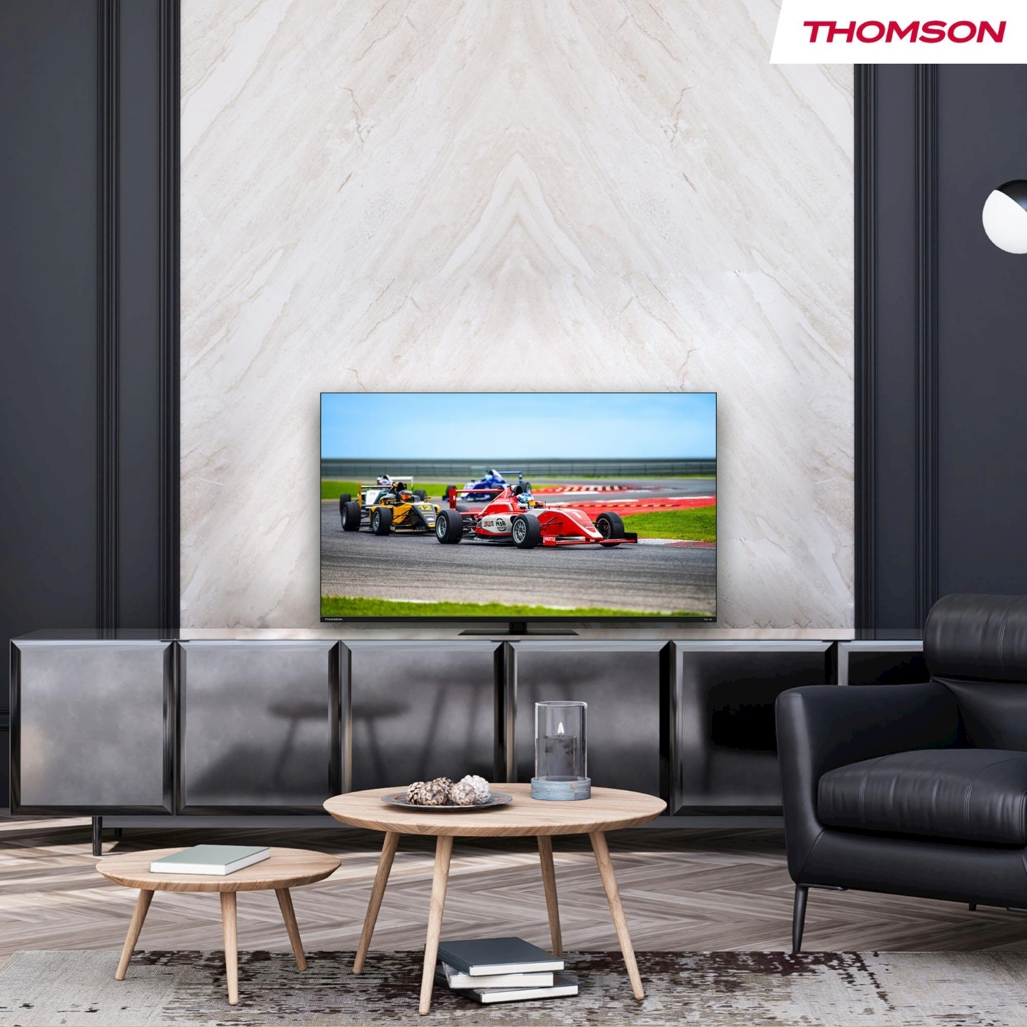 Soggiorno con TV con auto da corsa. Arredamento: divano, tavoli e mobile. Logo Thomson visibile.