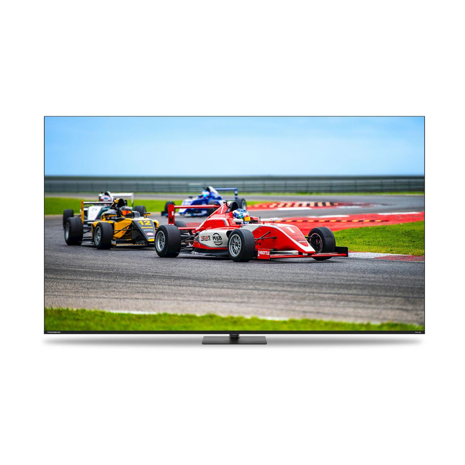 Auto da corsa di Formula 1 su pista. Auto rossa davanti, seguita da auto gialle e blu. Cielo blu chiaro sullo sfondo.