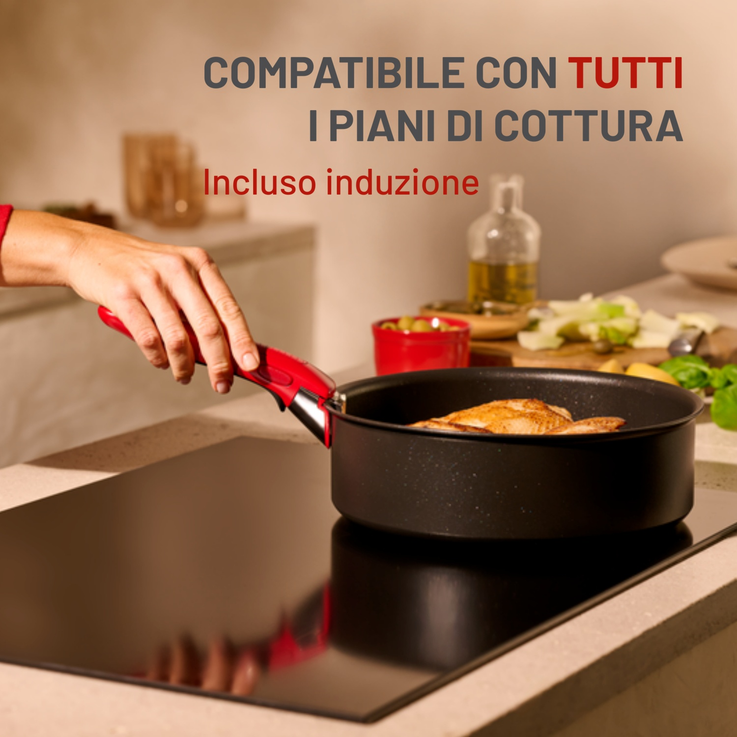 Una mano tiene una padella con manico rosso con cibo su un fornello nero. Il testo sopra dice: 'Compatibile con tutti i piani cottura'.
