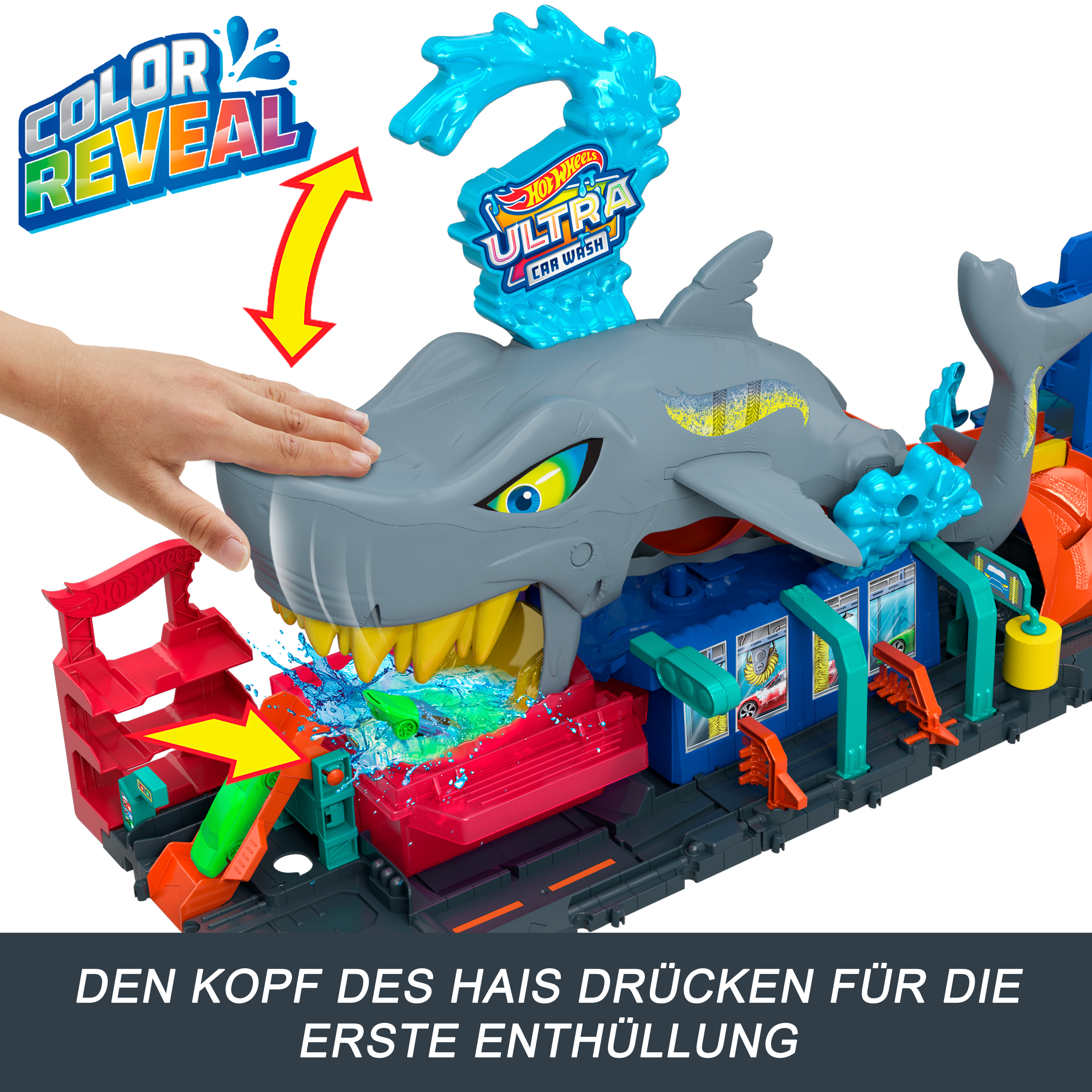 Ein haiförmiges Autowaschspielzeug. Eine Hand drückt den Haifischkopf. Das Spielzeug hat eine rote Rampe und ein grünes Auto.