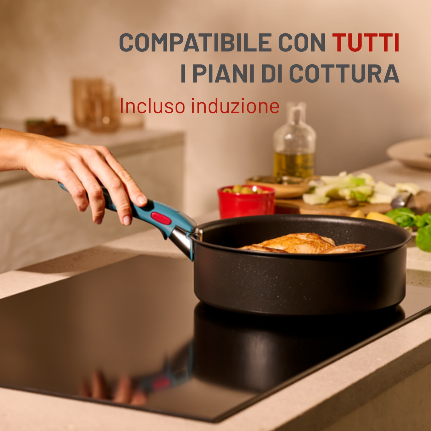Una mano tiene una padella su un fornello nero. La padella contiene cibo. Il testo in alto dice 'compatibile con tutti i piani cottura'.