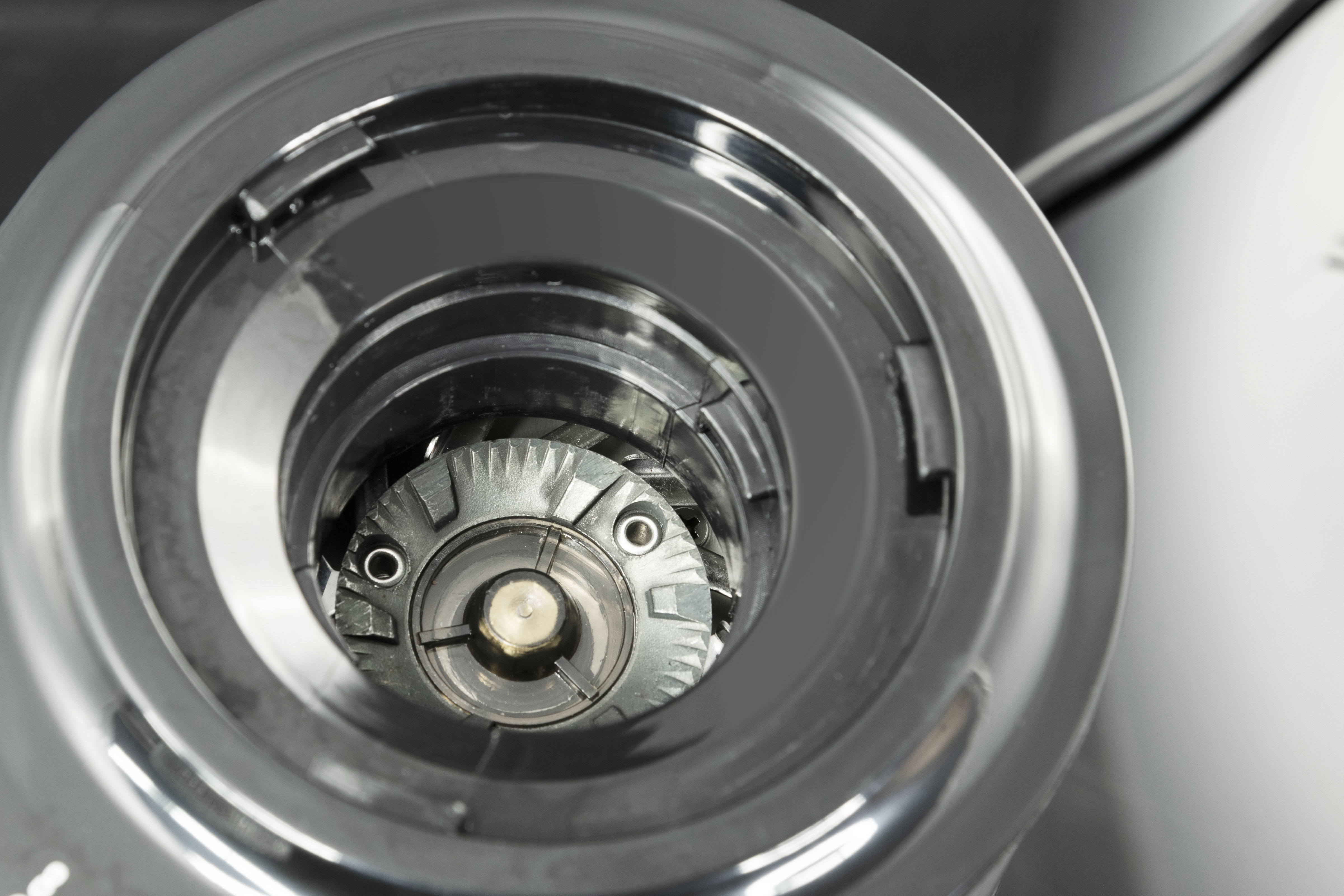 Zbliżenie wnętrza metalowego urządzenia, pokazujące okrągłą strukturę z ostrzami i metalowymi elementami.