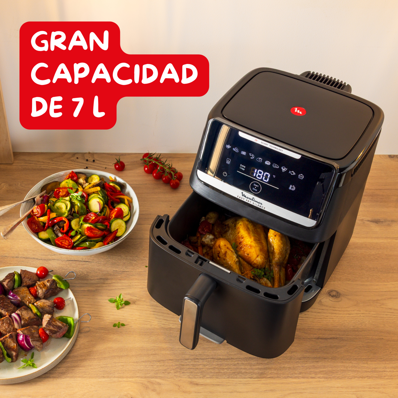 Una freidora de aire con pollo dentro, verduras y brochetas, sobre una mesa de madera. Texto rojo: 'GRAN CAPACIDAD DE 7 L'.