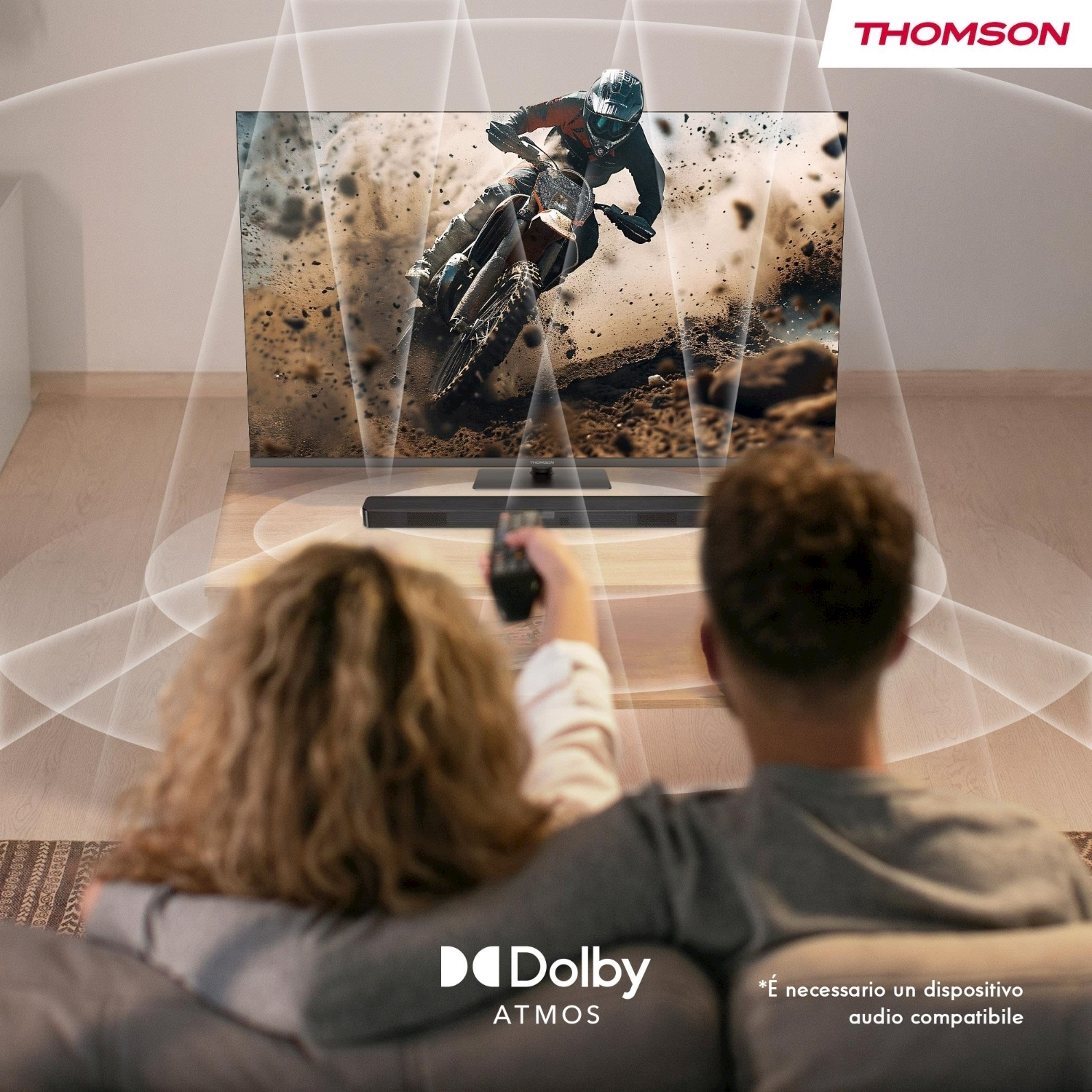 Una coppia guarda la TV che mostra una gara di motocross. La TV Thomson ha una soundbar. La stanza ha un logo Dolby Atmos.