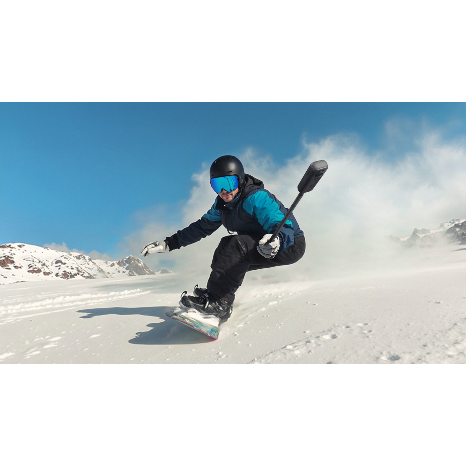 Snowboarder en action. Ciel bleu, neige blanche et montagnes en arrière-plan. La personne porte un casque, des lunettes et une veste bleue et noire.