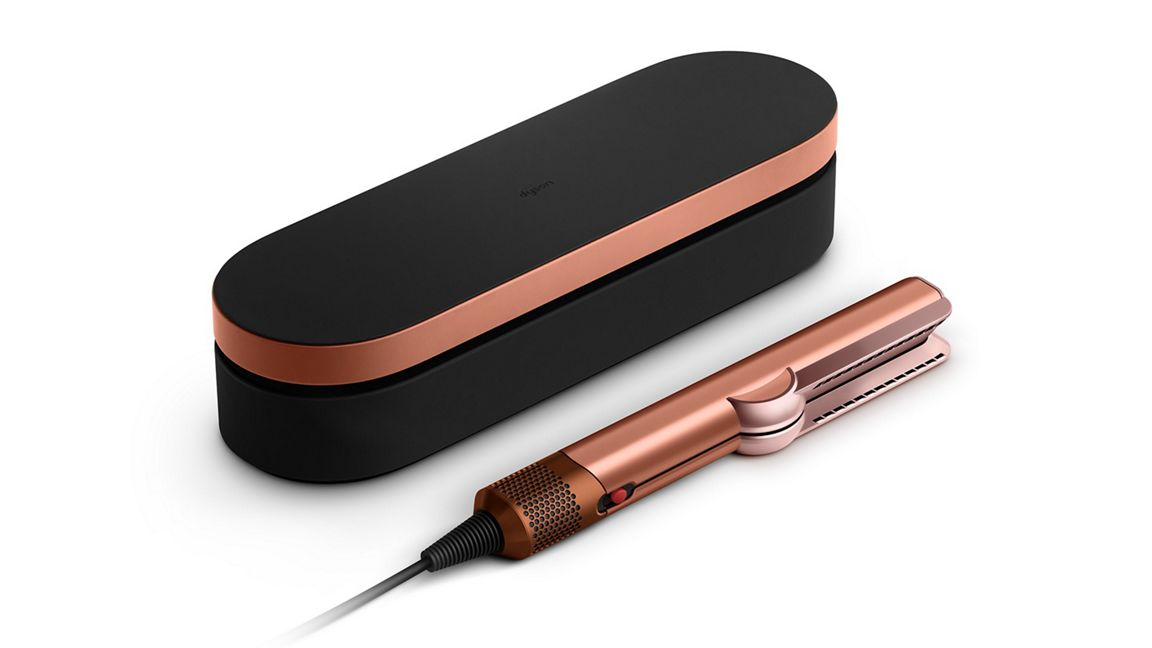 Una plancha de pelo oro rosa y un estuche negro con ribete oro rosa sobre una superficie blanca. La plancha tiene un cable.