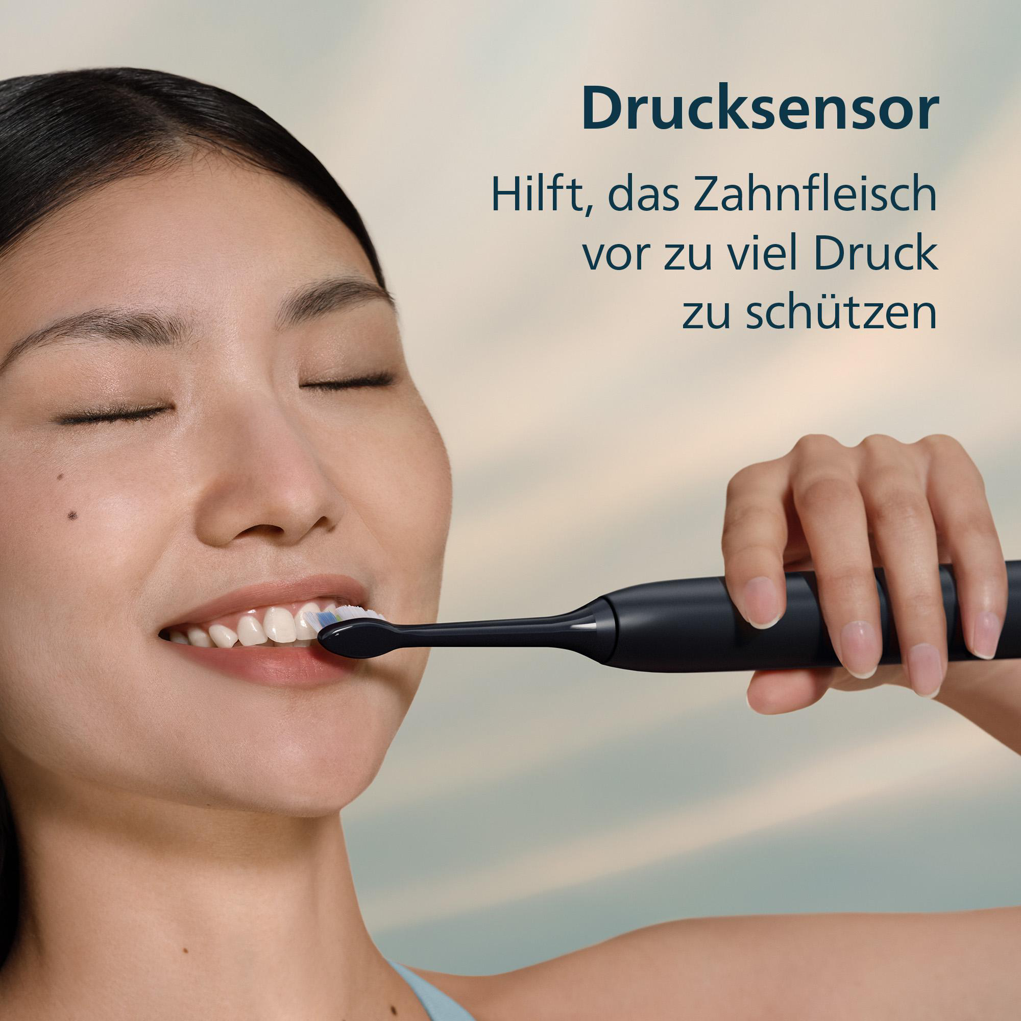 Frau putzt Zähne mit schwarzer Zahnbürste. Text: Drucksensor, schützt das Zahnfleisch. Hintergrund hellblau.