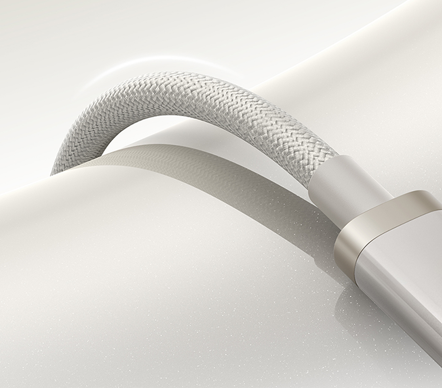 Primer plano de un cable trenzado blanco que se curva sobre una superficie blanca reflectante, terminando con un conector plateado.