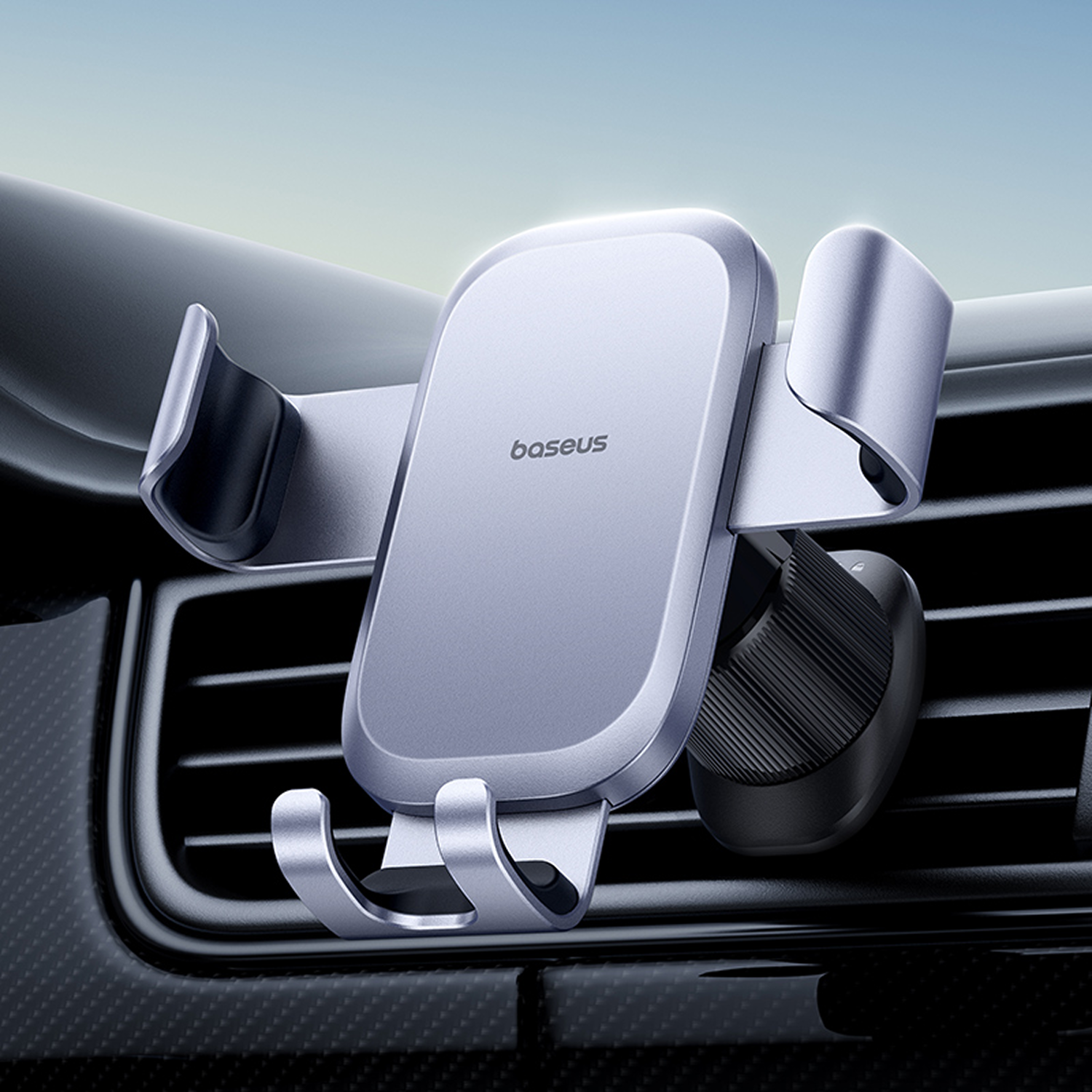 Un soporte plateado para teléfono de coche Baseus montado en una rejilla de ventilación del coche. El soporte no sostiene nada. El fondo está borroso.