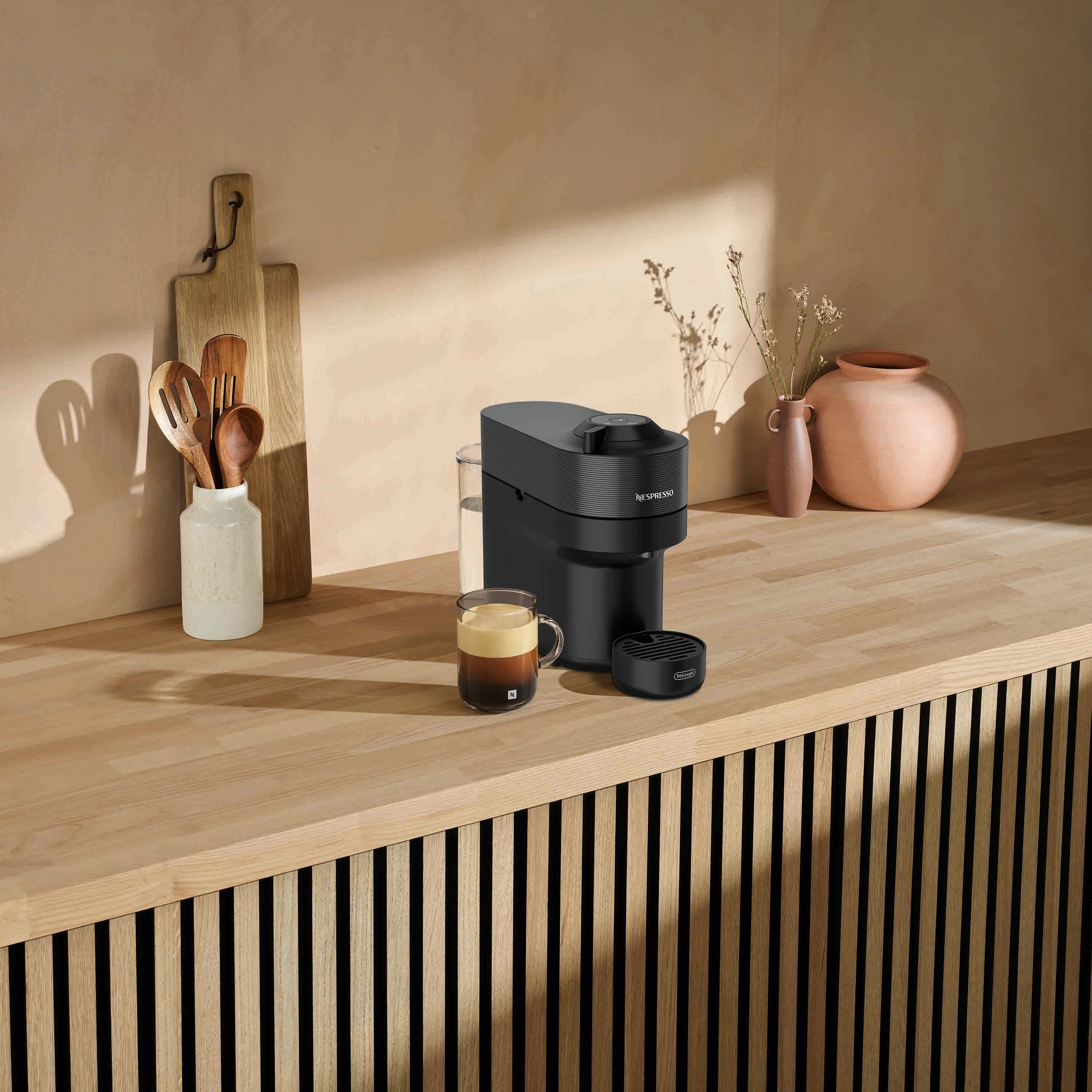 Macchina da caffè con una tazza di caffè su un bancone di legno, con utensili di legno e un vaso.
