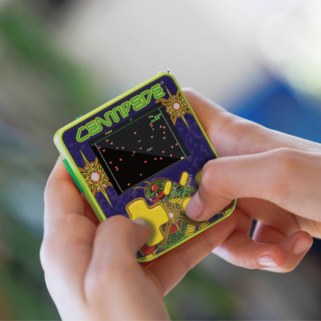 Manos sosteniendo una consola de juegos Centipede retro. La pantalla muestra un juego. La consola es verde, morada y amarilla.