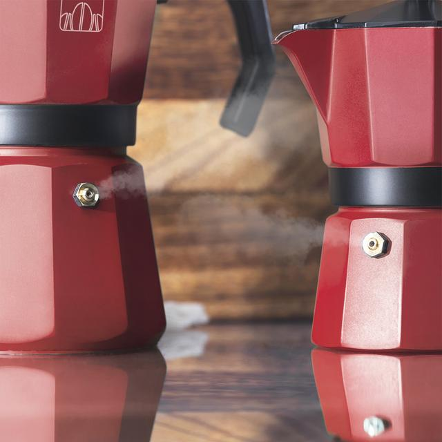 Dos cafeteras rojas con vapor. Una a la izquierda, otra a la derecha. Ambas sobre superficie de madera.