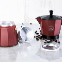 Una cafetera moka roja con tapa y base negras, un tarro de cristal y granos de café sobre una superficie blanca.