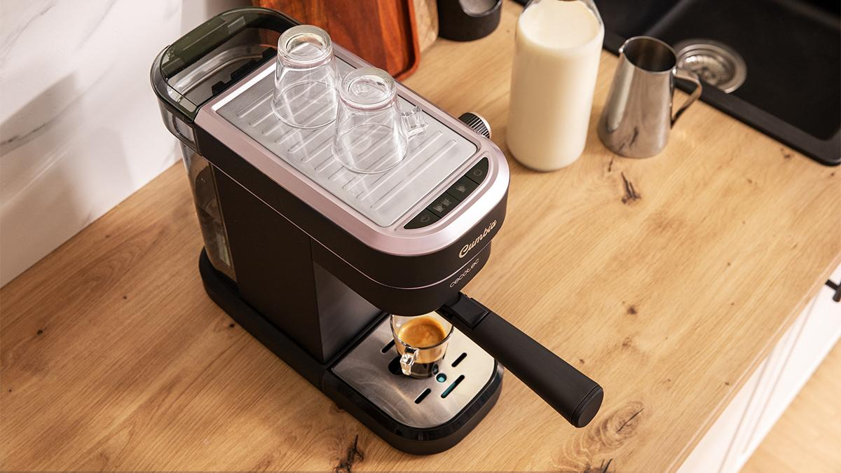 Máquina de espresso sobre superficie de madera. Se está haciendo un vaso de café. Botella de leche y jarra a la derecha.