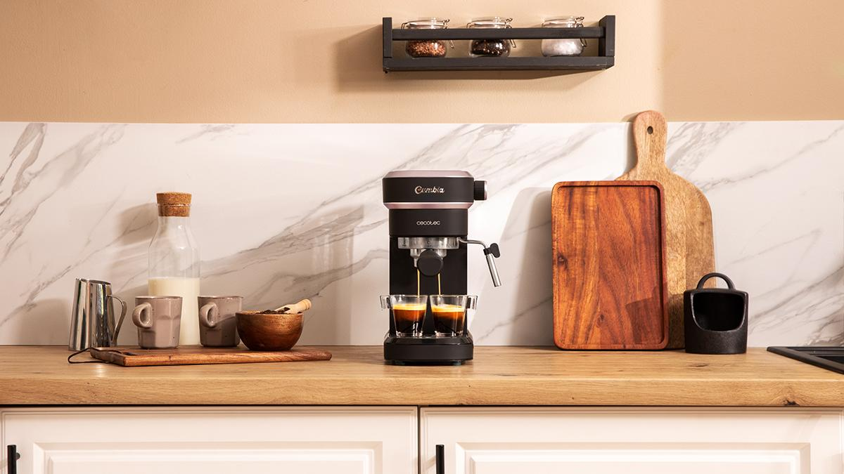 Cafetera dispensando espresso en dos vasos. Encimera de cocina con leche, tazas y tablas de cortar.