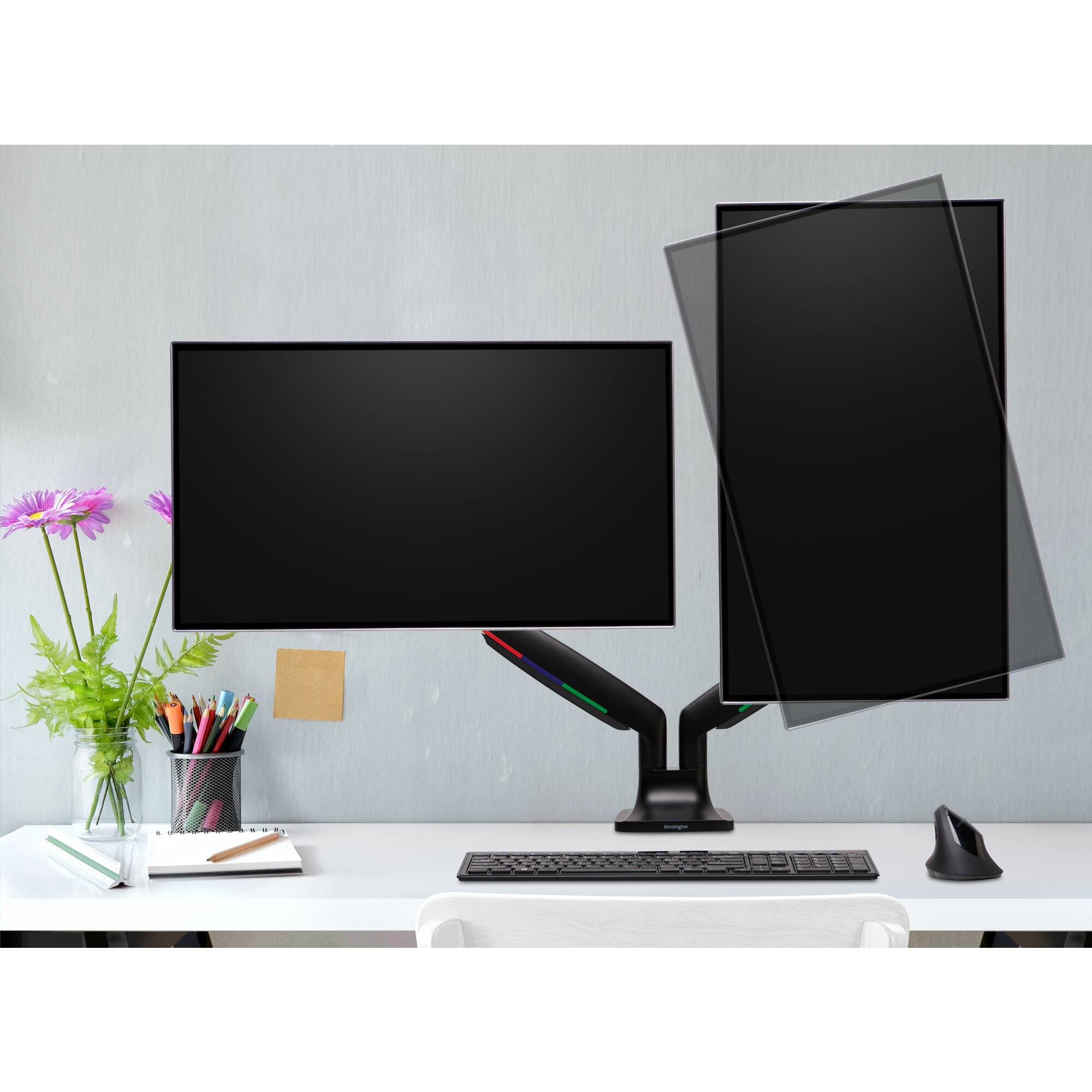 Schreibtisch-Setup mit zwei Monitoren, Tastatur, Maus und Blumen. Die Anzeigen sind schwarz, vor einer hellgrauen Wand.
