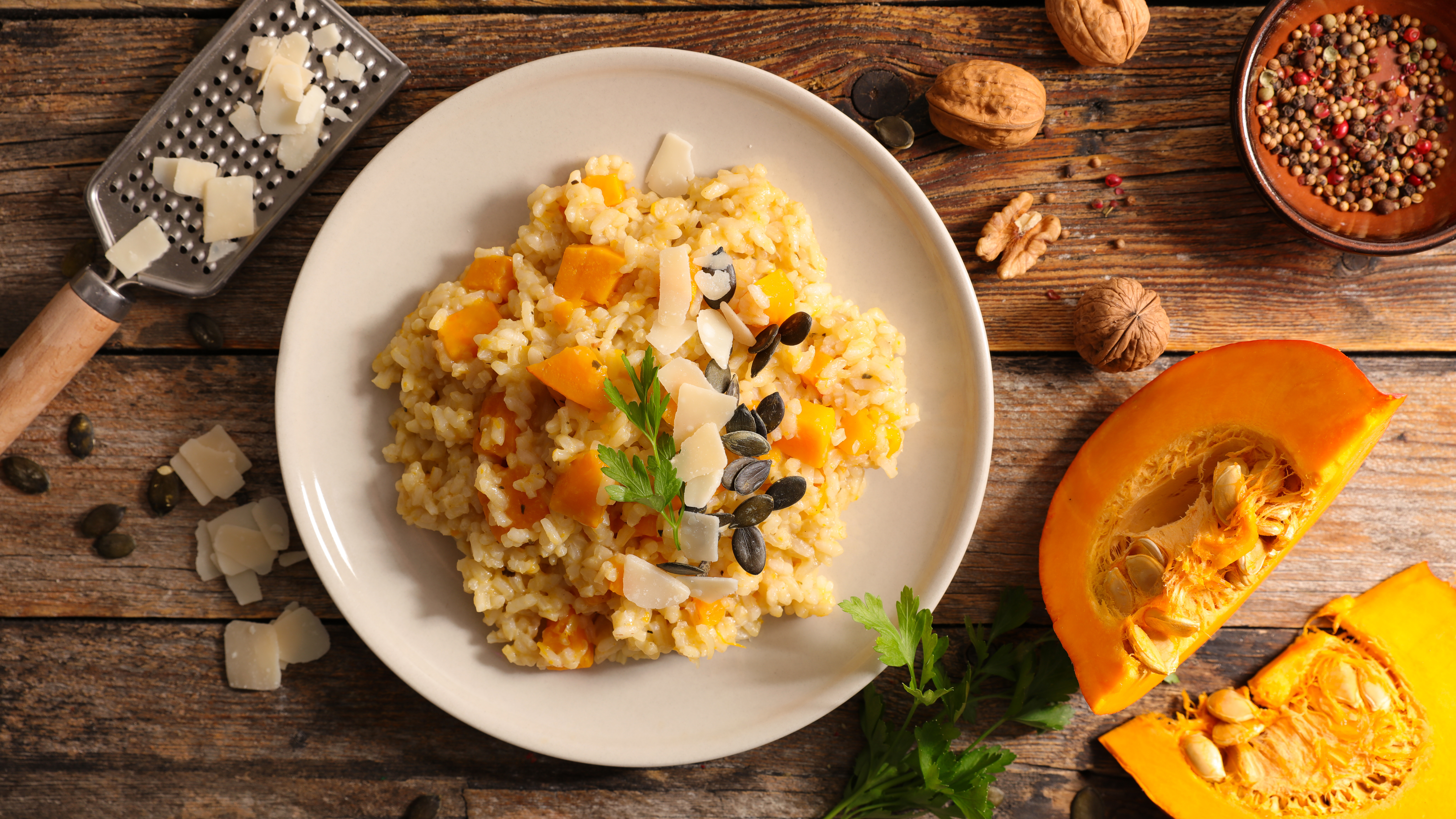 Draufsicht auf Risotto mit Kürbis, Samen und Parmesan auf einem Teller, mit Walnüssen, Gewürzen und Kürbisscheibe.