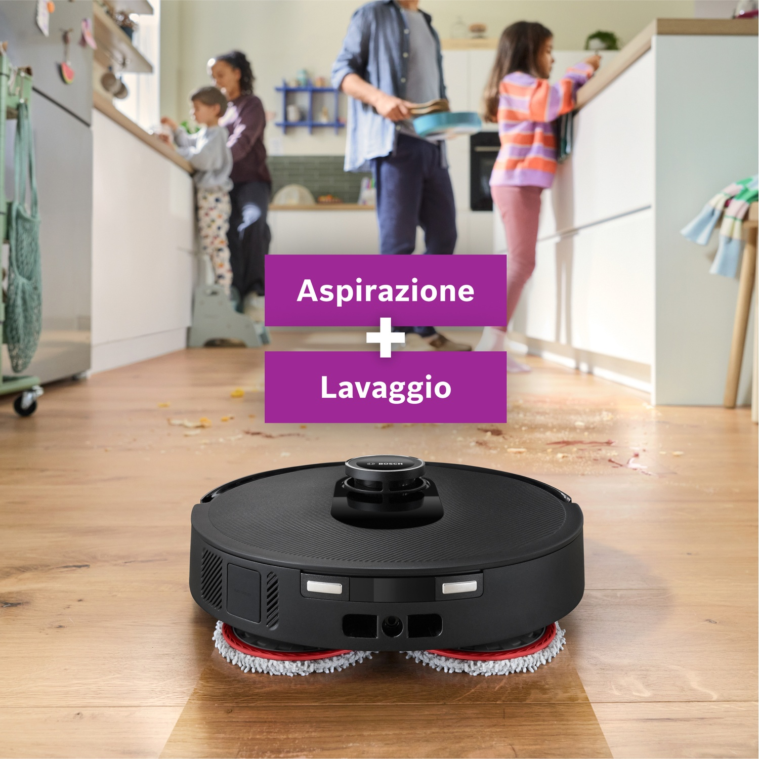 Un aspirapolvere robot nero su un pavimento in legno. Sullo sfondo, una famiglia in cucina. Testo: Aspirazione + Lavaggio.